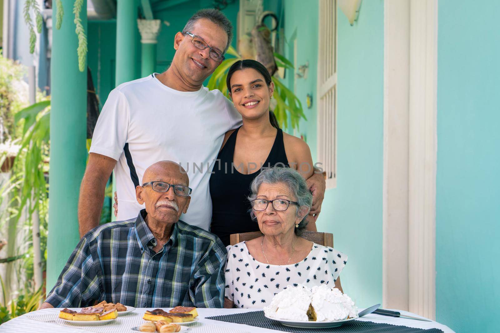 Elderly couple wearing eyeglasses sitting at a table and a man and a young woman standing behind the elderly