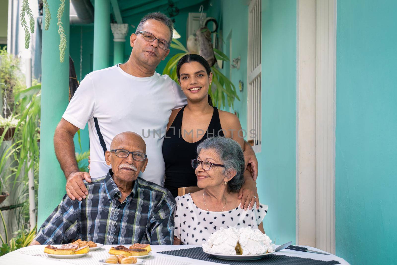 Elderly couple wearing eyeglasses sitting at a table and a man and a young woman standing behind the elderly