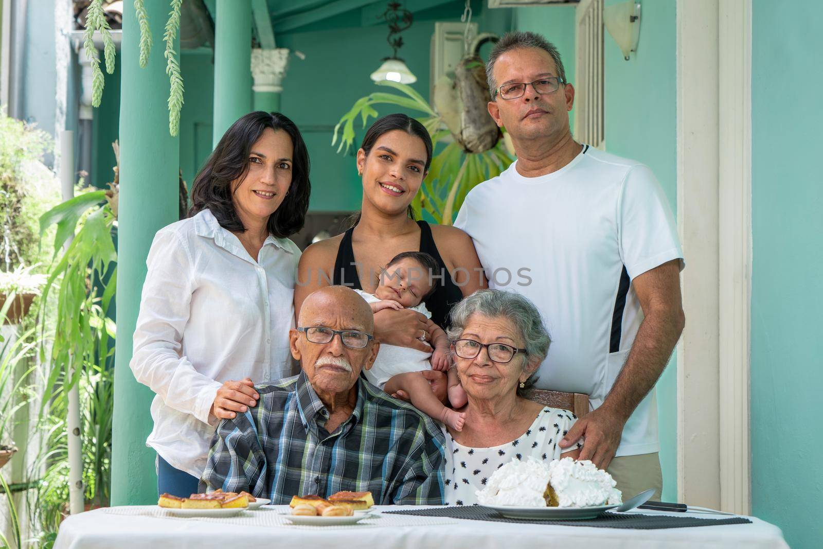 Elderly couple sitting. A man a woman and a young woman with a child in their arms standing behind the elderly couple