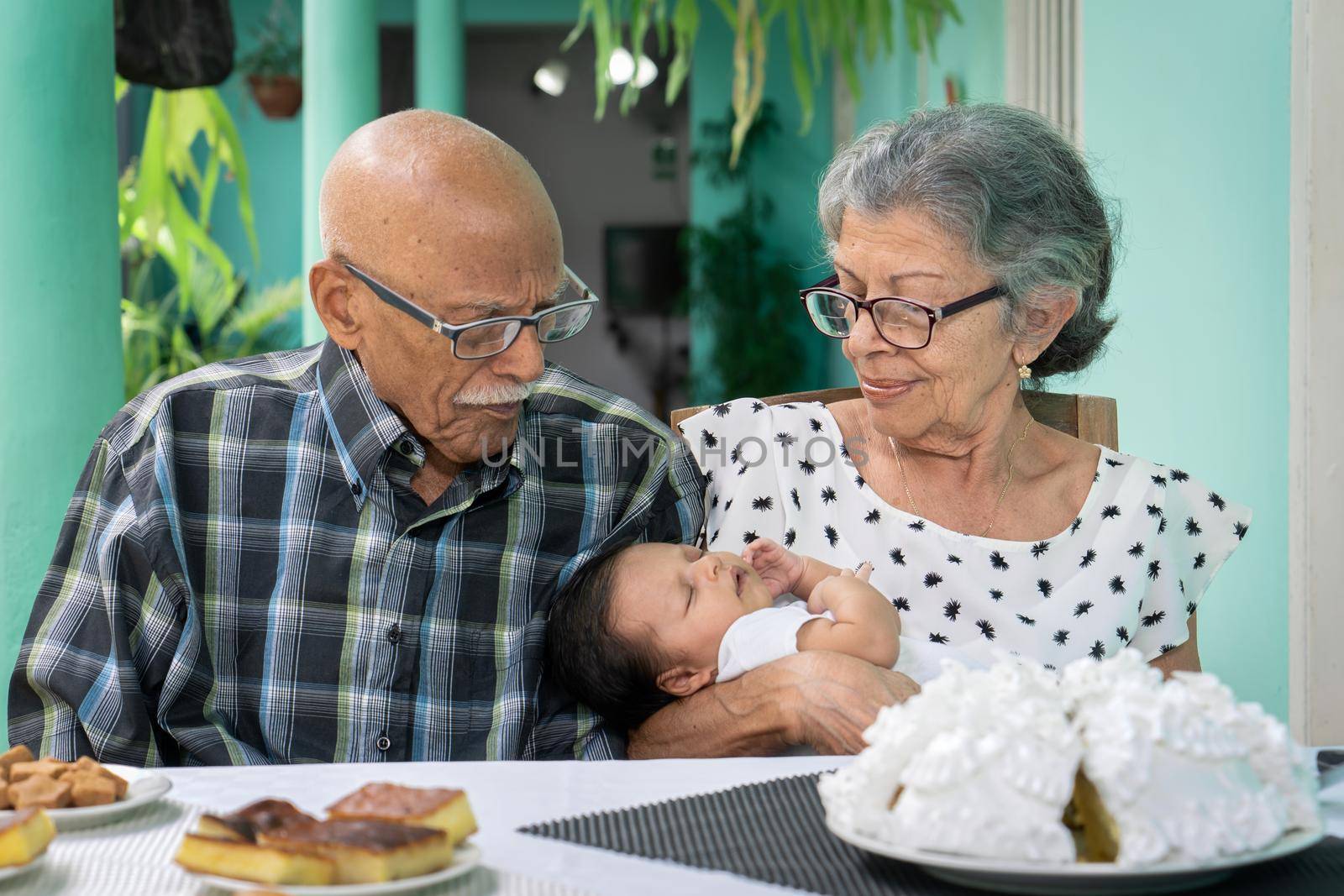 Elderly couple sitting at a table with an infant in the woman's arms