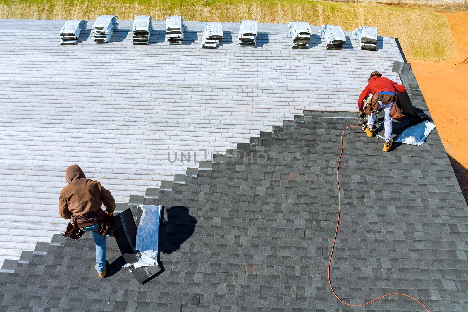 Worker hands installing bitumen roof shingles with air hammer and nail by ungvar