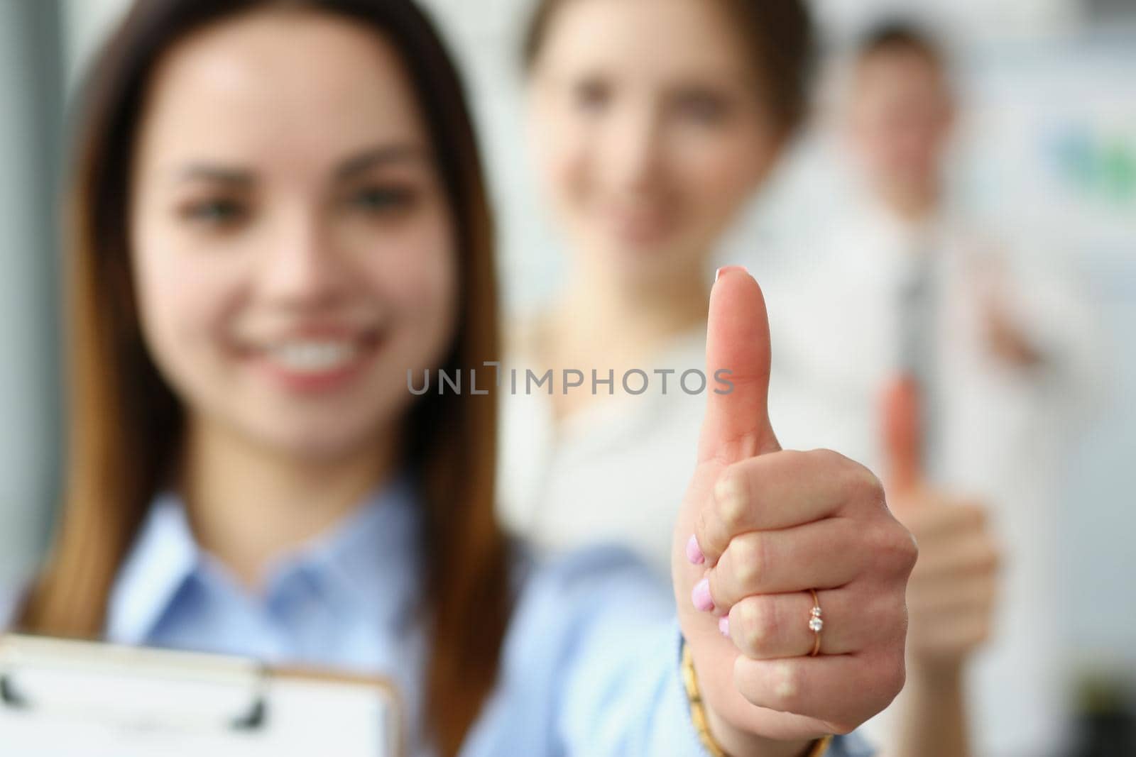 Close-up of smiling female showing thumbs up and confirm success on camera. Business partners posing in company office. Business, goal, good job concept