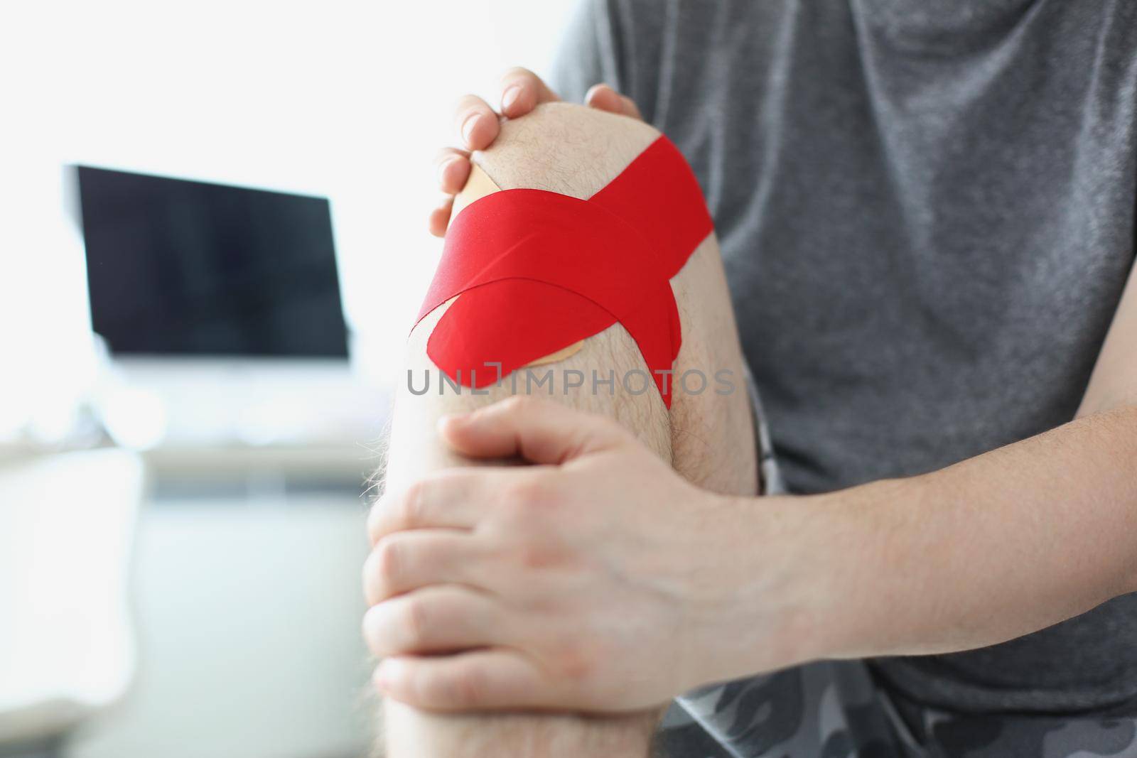 Close-up of man sit in hospital with kinesiology tape on knee, pain in leg, rehabilitation after injury, qualified help. Physical therapy, health concept