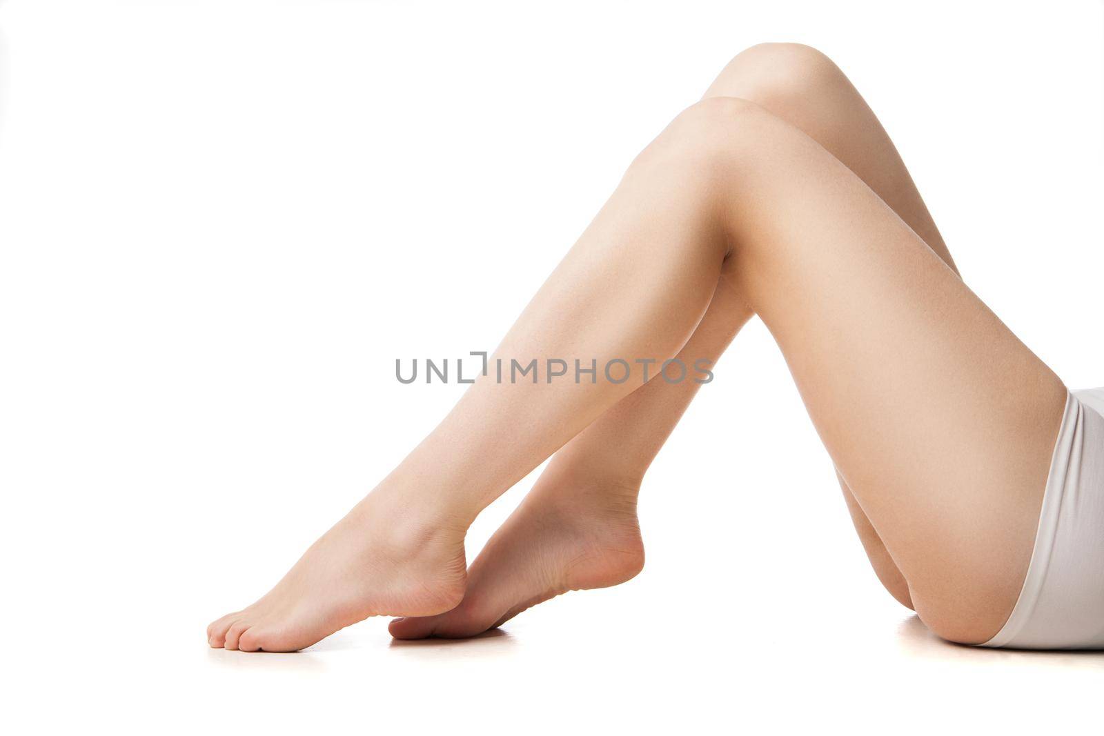 Close-up of young woman with beautiful legs lying against white background