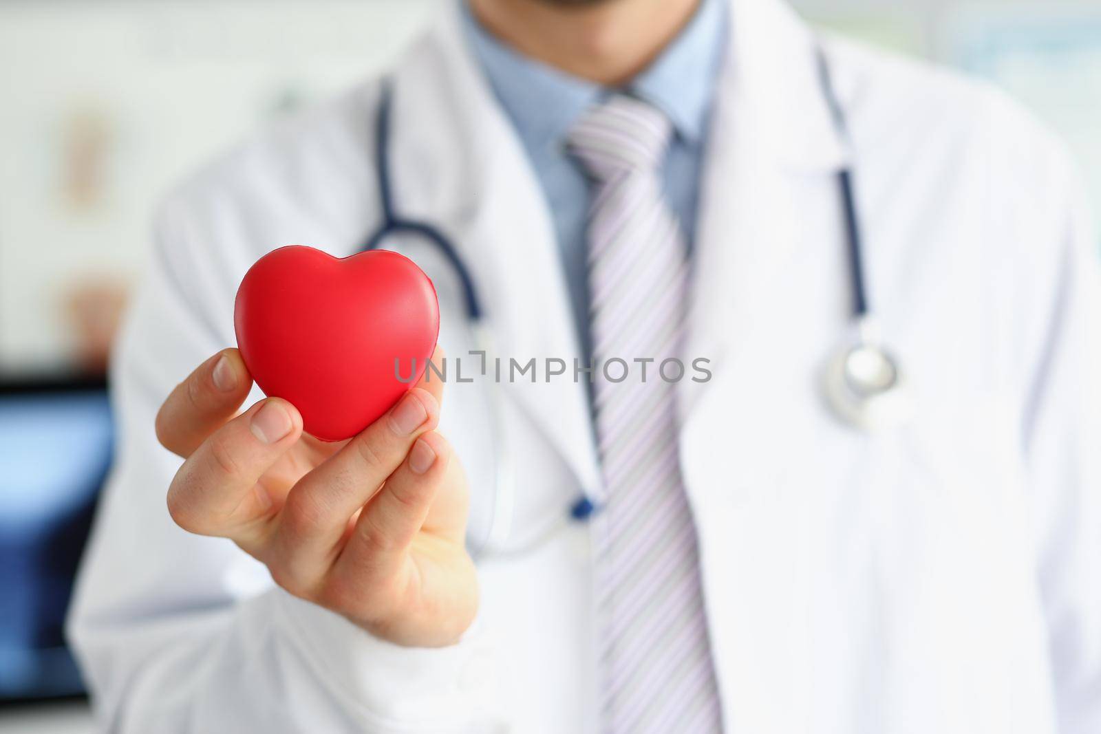 Close-up of man doctor hold red plastic heart and posing with stethoscope on neck. Save life through body checkup. Medicine, cardiology, healthcare concept