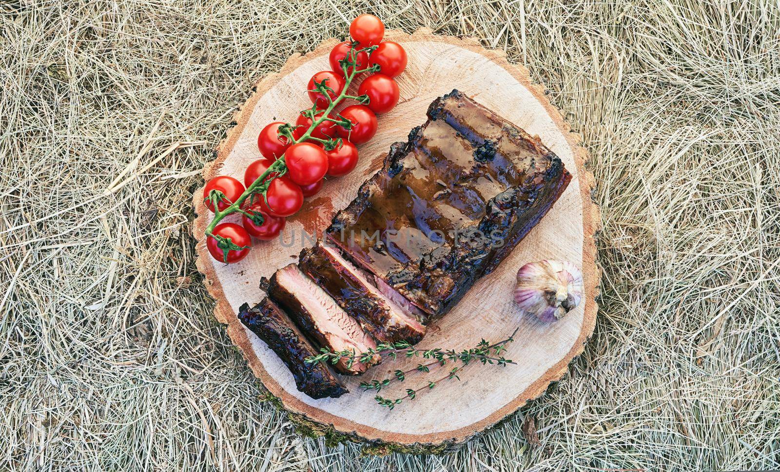 Barbecue ribs meat prepared in traditional European style with rosemary herb cherry tomatoes and garlic on a raw solid wood cutting plate