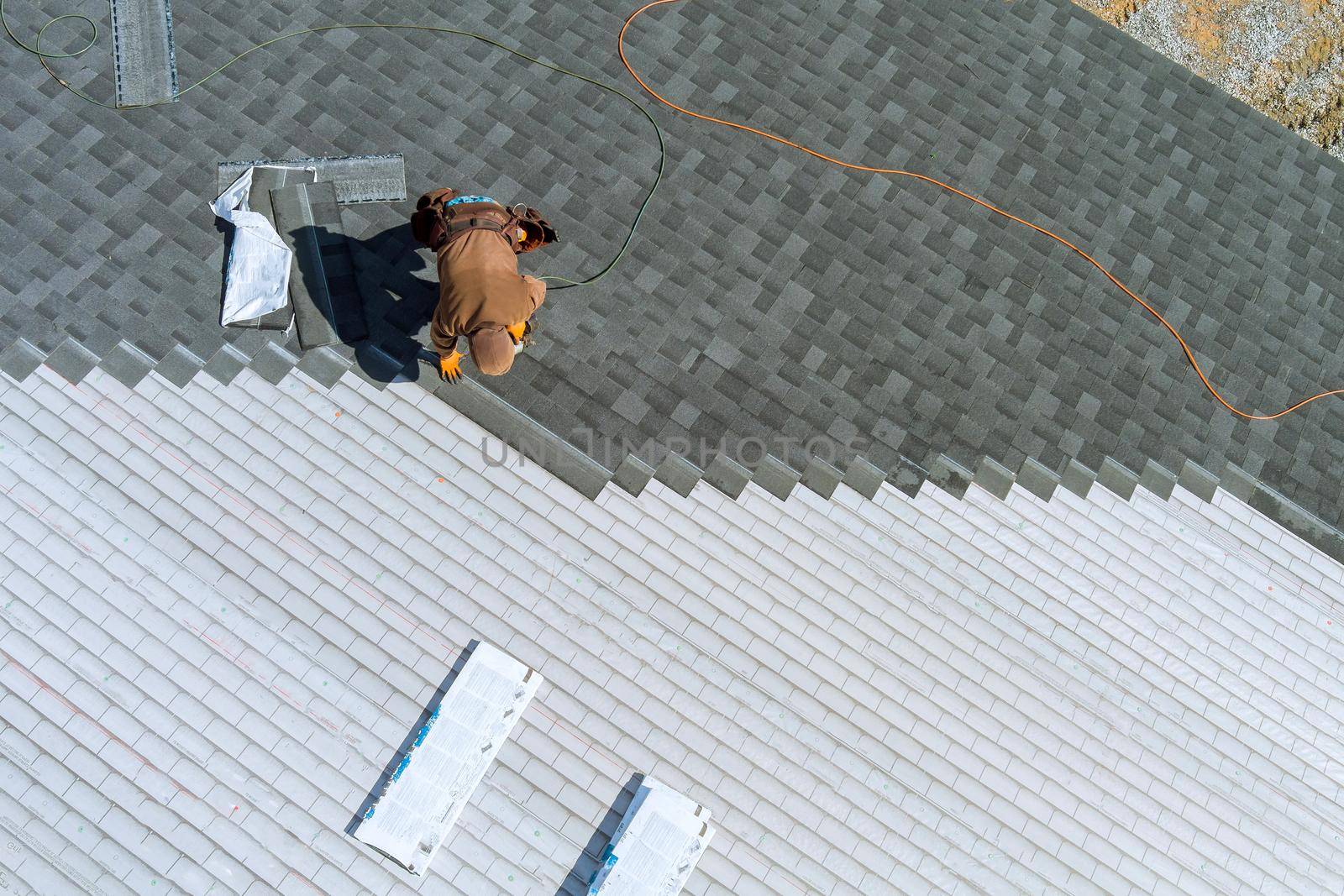 A worker installing shingles on the roof of a home with air hammer and nails