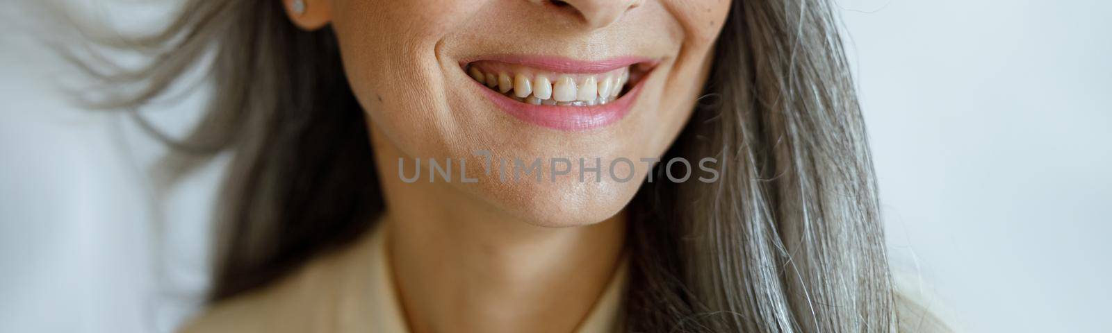 Joyful middle aged Asian female model with flying silver hair on light grey background by Yaroslav_astakhov