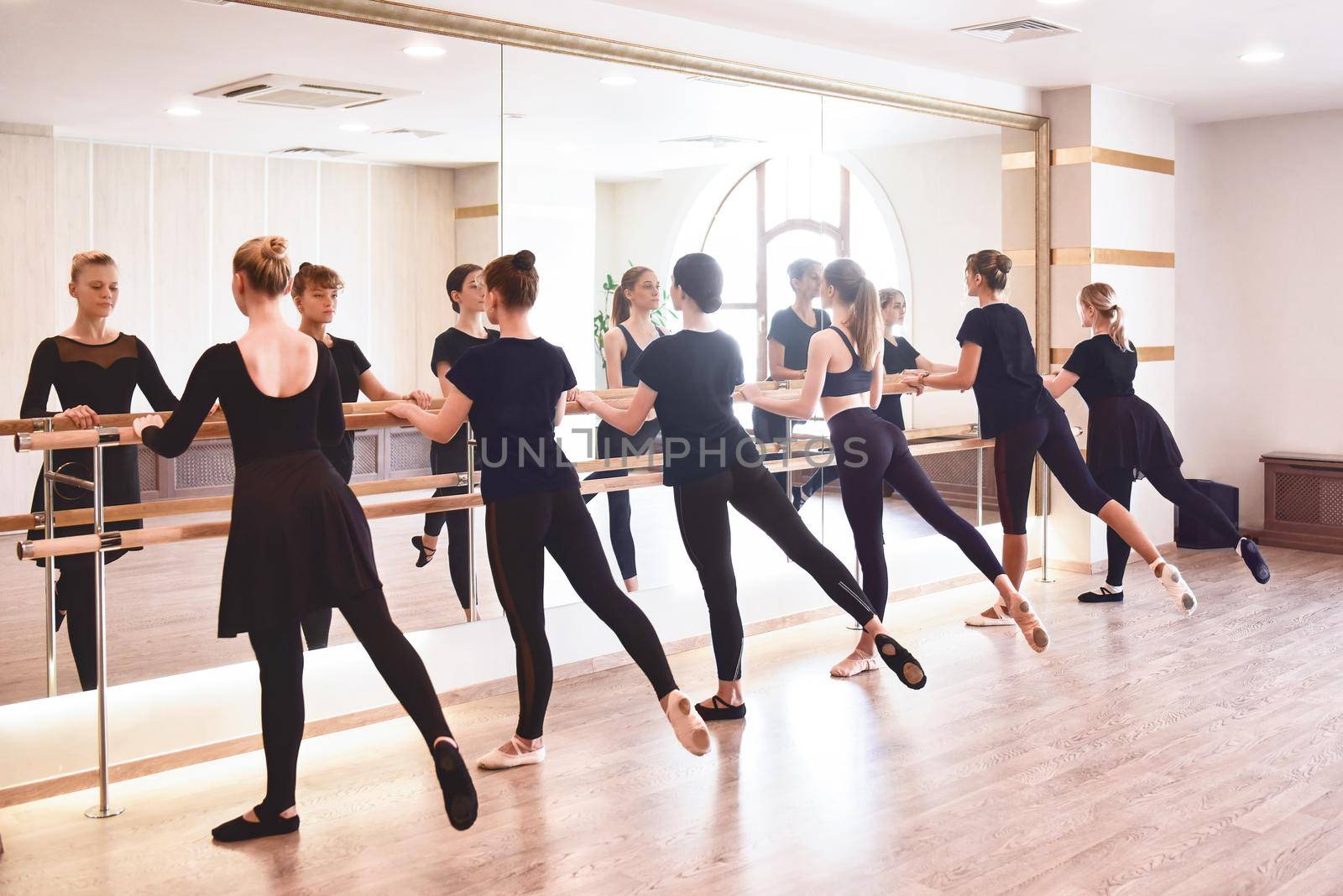 Group of people doing exercises using barre in gym with focus to fit athletic toned .woman in foreground in health and fitness concept. by Nickstock
