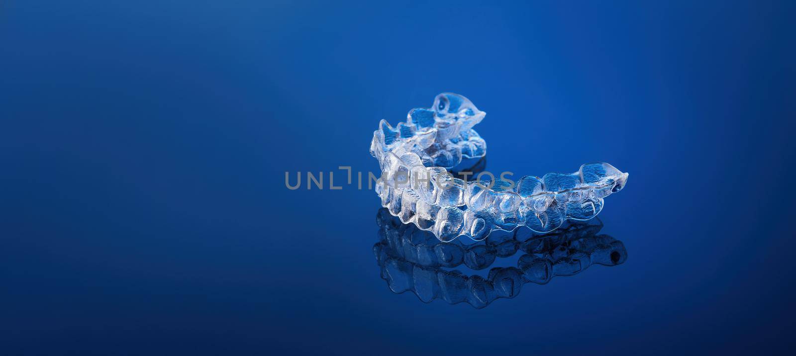 Invisible orthodontics cosmetic brackets on blue gradient background, tooth aligners, plastic braces. A way to have a beautiful smile and white teeth. by EvgeniyQW