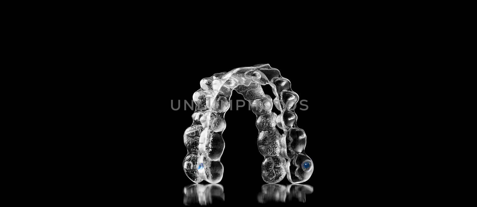 Invisible orthodontics cosmetic brackets on black background, tooth aligners, plastic braces. Modern teeth retainers created on a 3d printer. A way to have a beautiful smile and white teeth. by EvgeniyQW