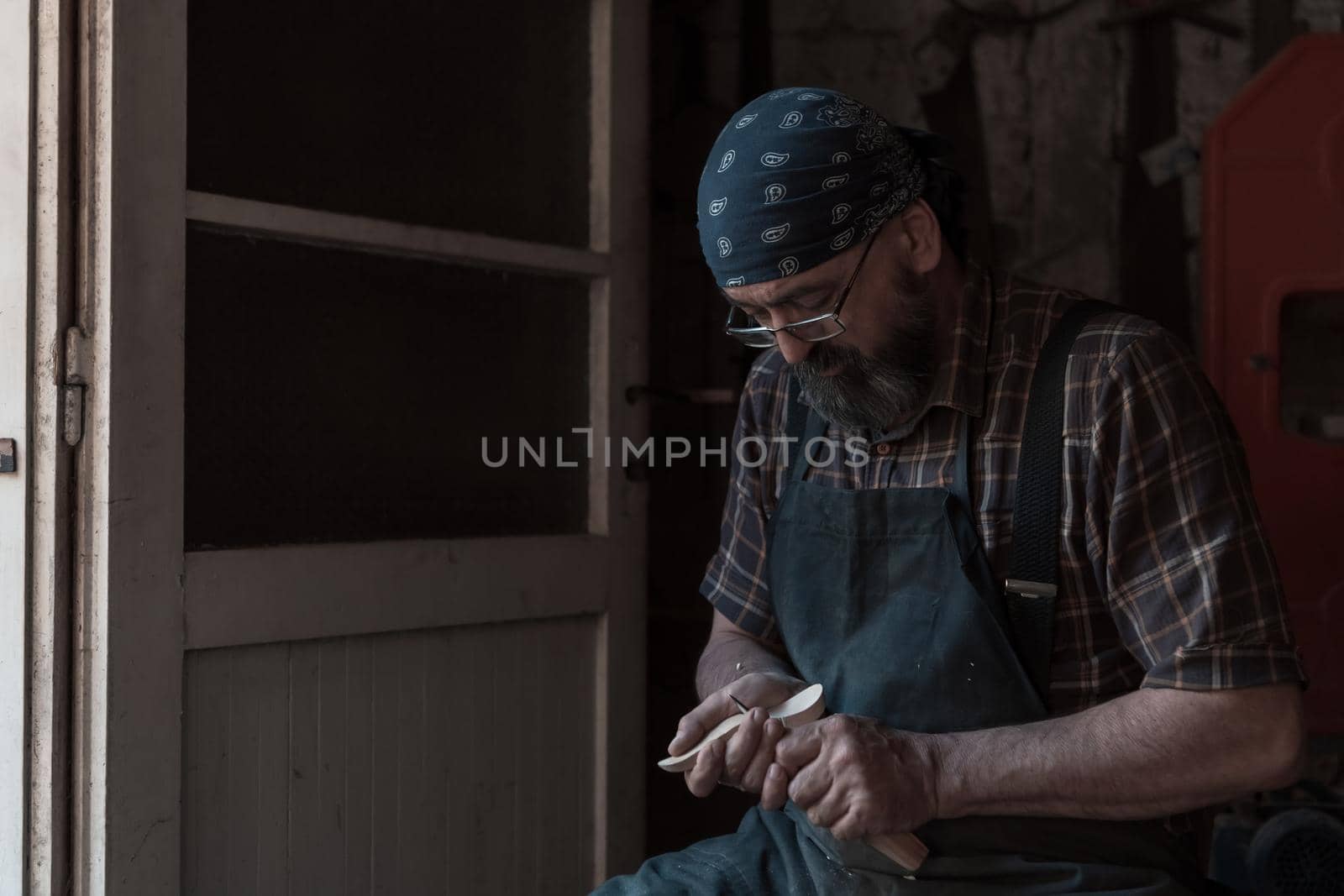 Spoon craft master in his workshop with handmade wooden products and tools working checking curve and line straight. High quality photo