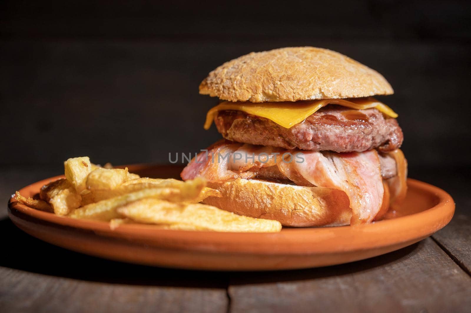 Premium grilled beef hamburger with bacon, cheese and French fries. Delicious American burger on wooden background. by HERRAEZ