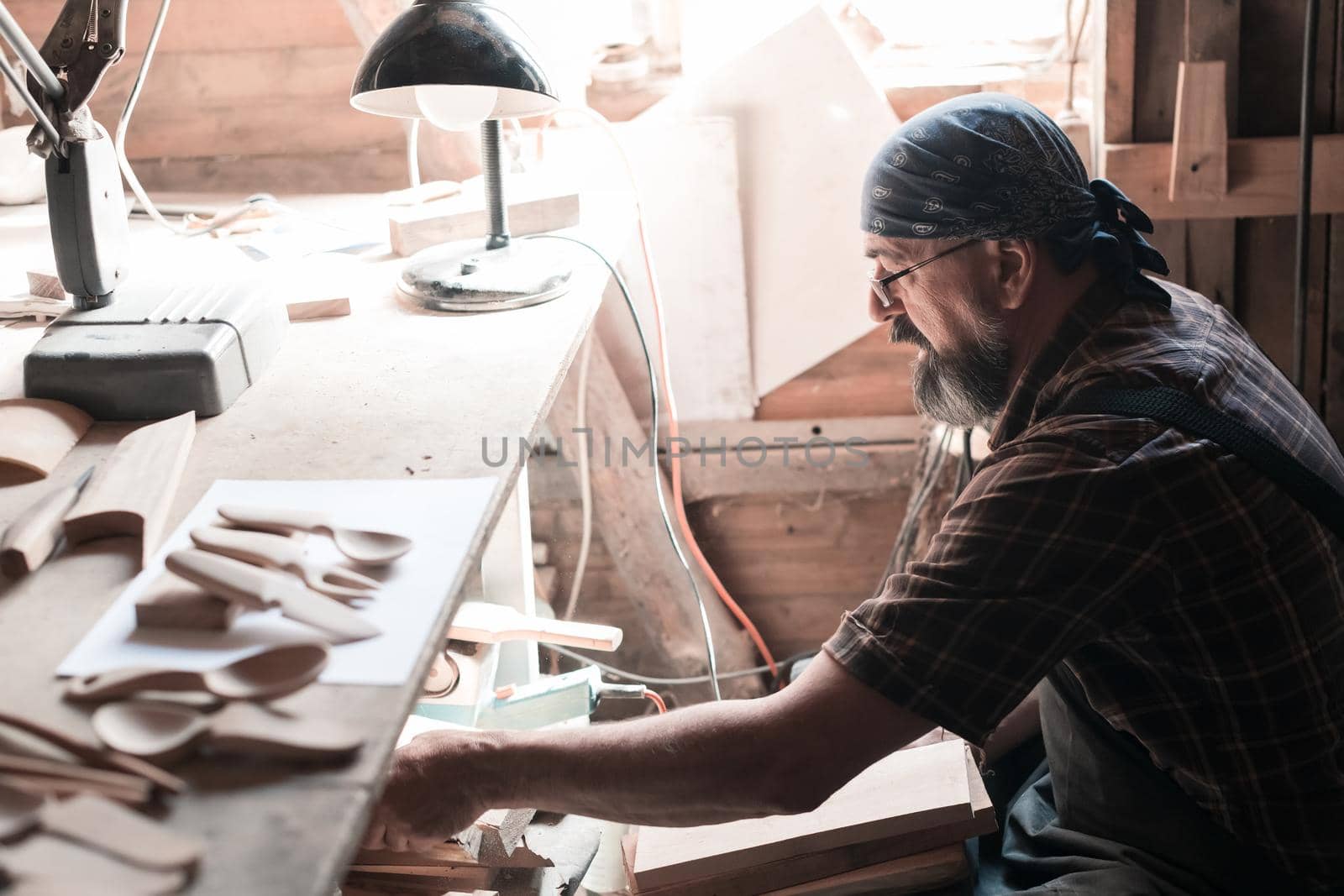 Spoon master in his workshop with wooden products and tools selecting right wood to make wooden kitchenware products. High quality photo