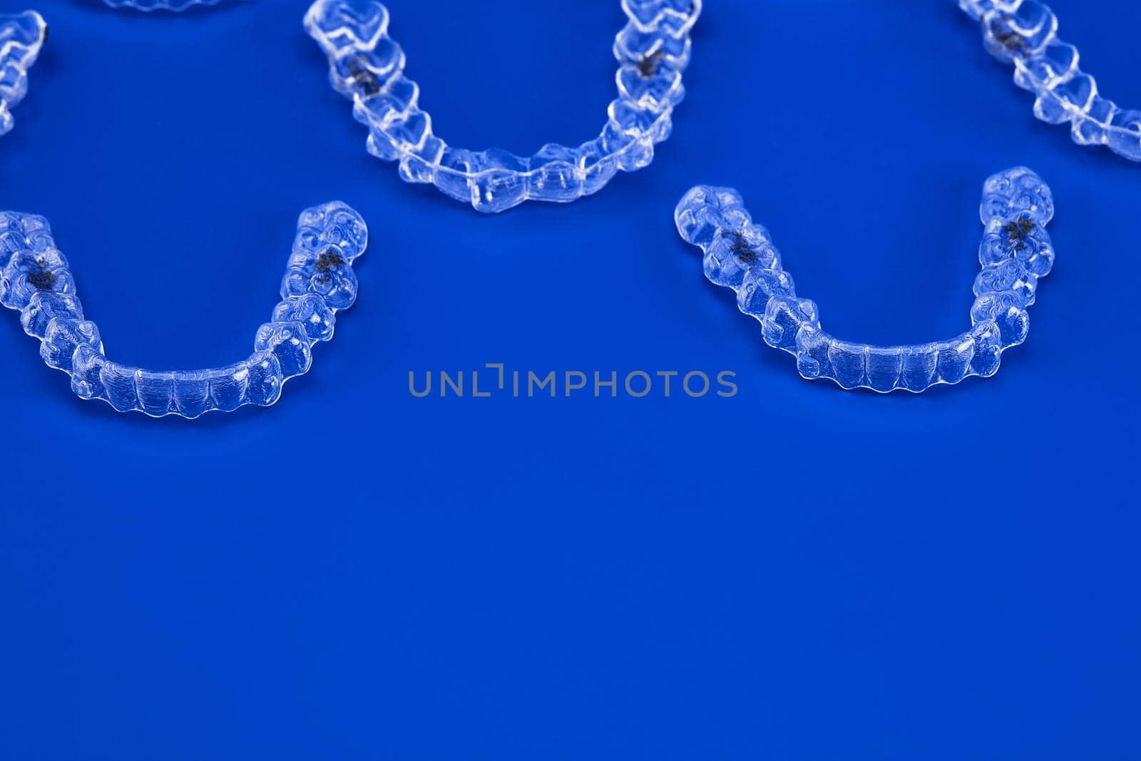 Invisible orthodontics cosmetic brackets on blue background, tooth aligners, plastic braces. A way to have a beautiful smile and white teeth.