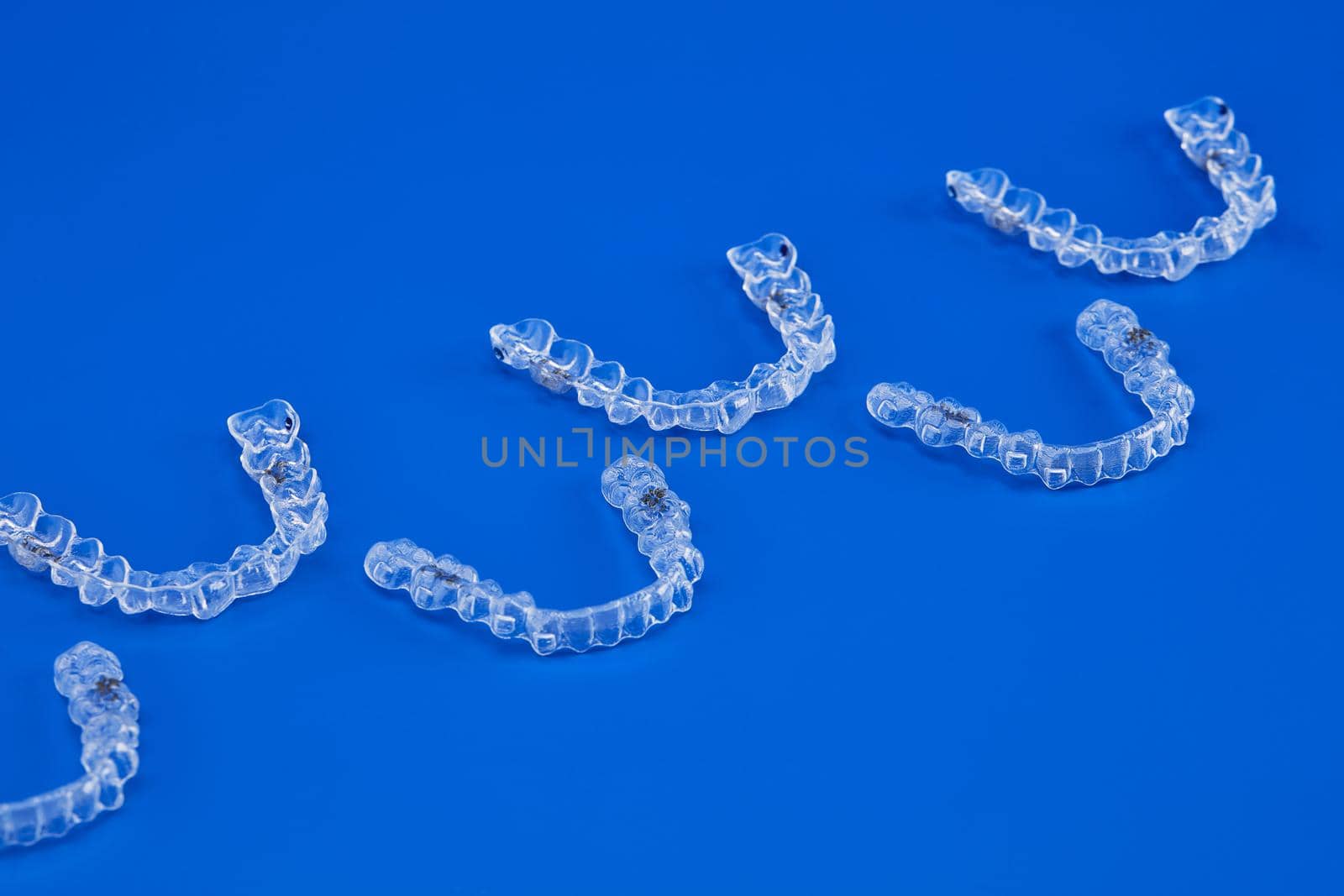Invisible orthodontics cosmetic brackets on blue background, tooth aligners, plastic braces. A way to have a beautiful smile and white teeth.
