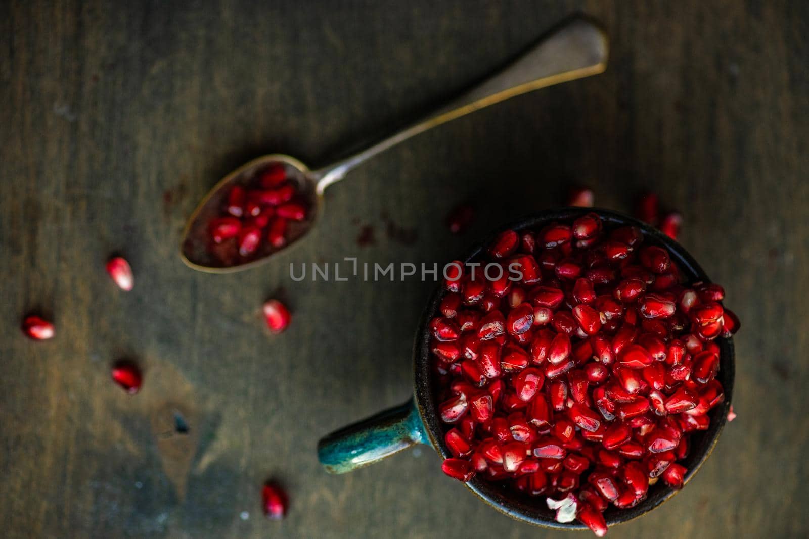 Ripe organic pomegranate fruit on the ceramic cup and vintage spoon on wooden table