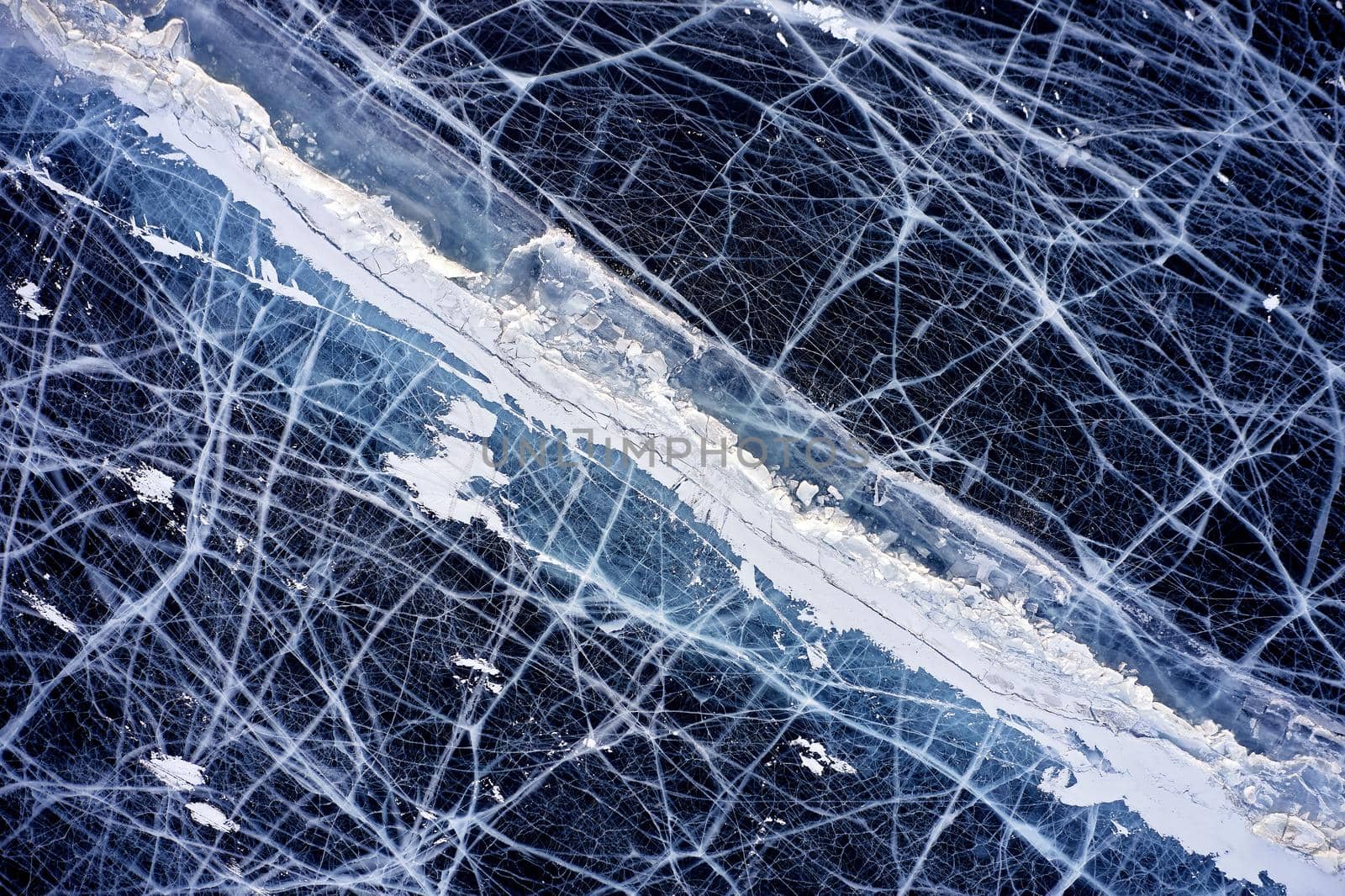 Frozen Lake Baikal, Aerial view. Beautiful winter landscape with clear smooth ice. Famous natural landmark Russia. Blue transparent ice with deep cracks, top view of a frozen lake.