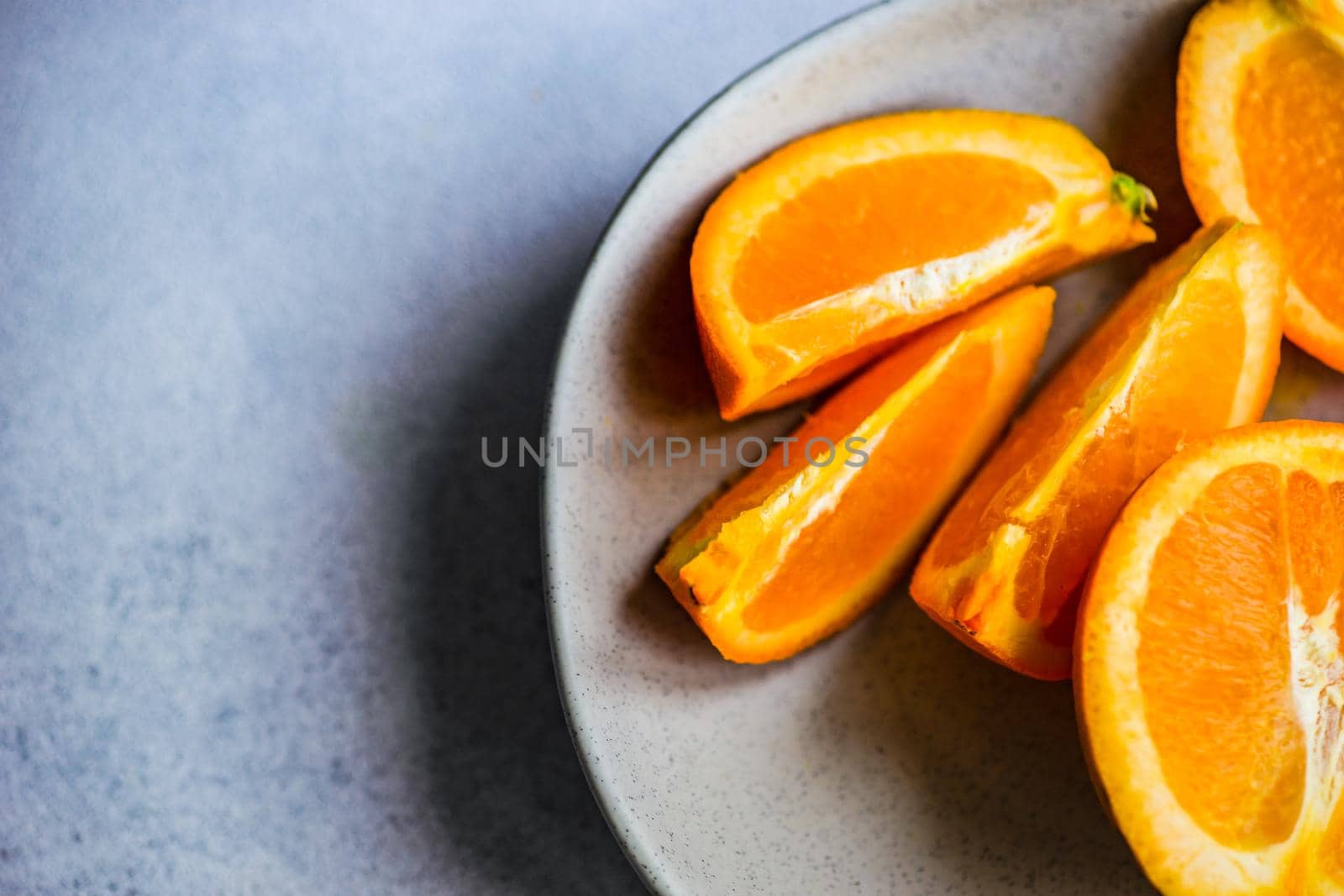 Slices of ripe orange fruits in the stone bowl on grey concrete background