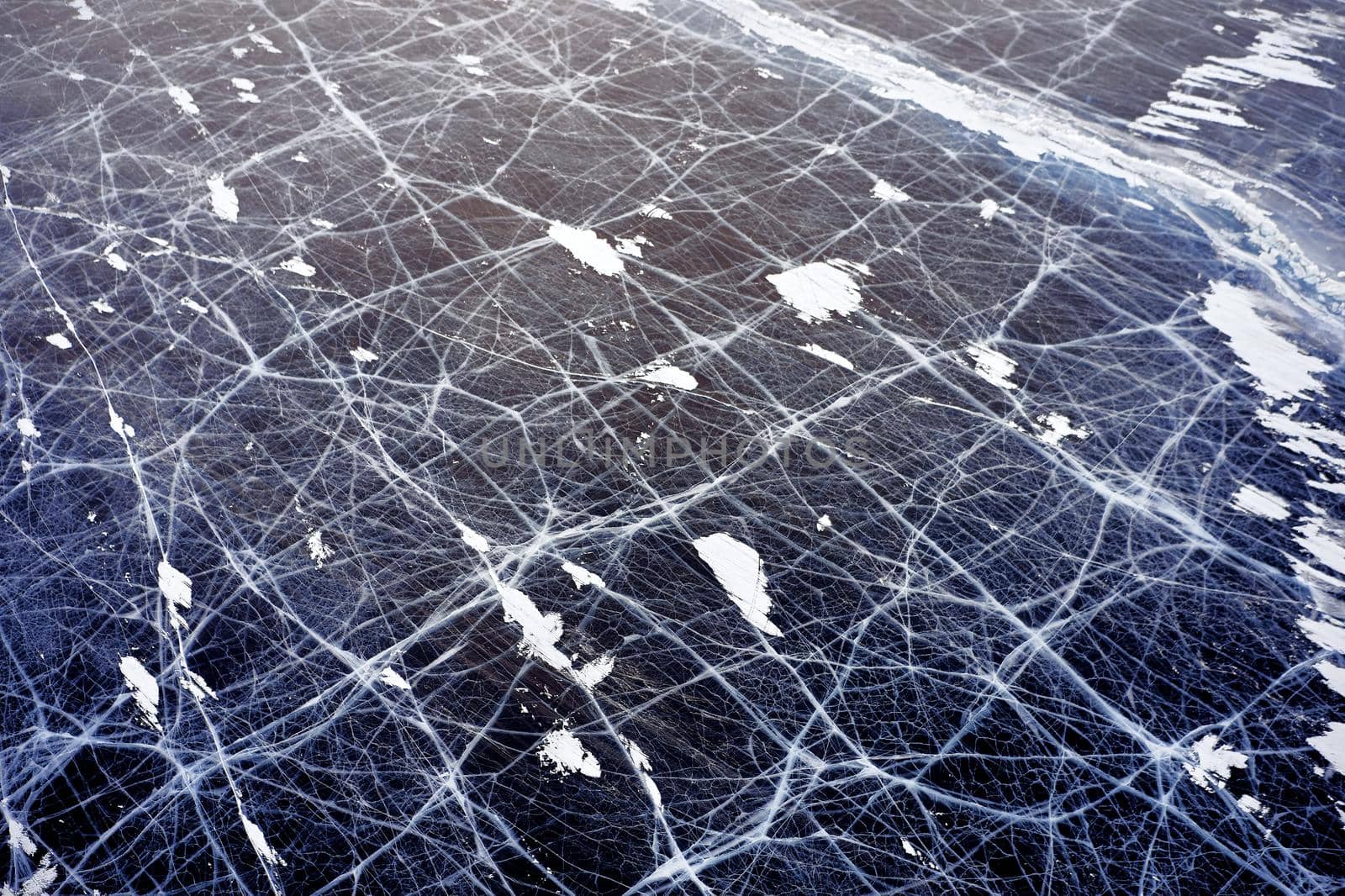 Frozen Lake Baikal, Aerial view. Beautiful winter landscape with clear smooth ice. Famous natural landmark Russia. Blue transparent ice with deep cracks, top view of a frozen lake.