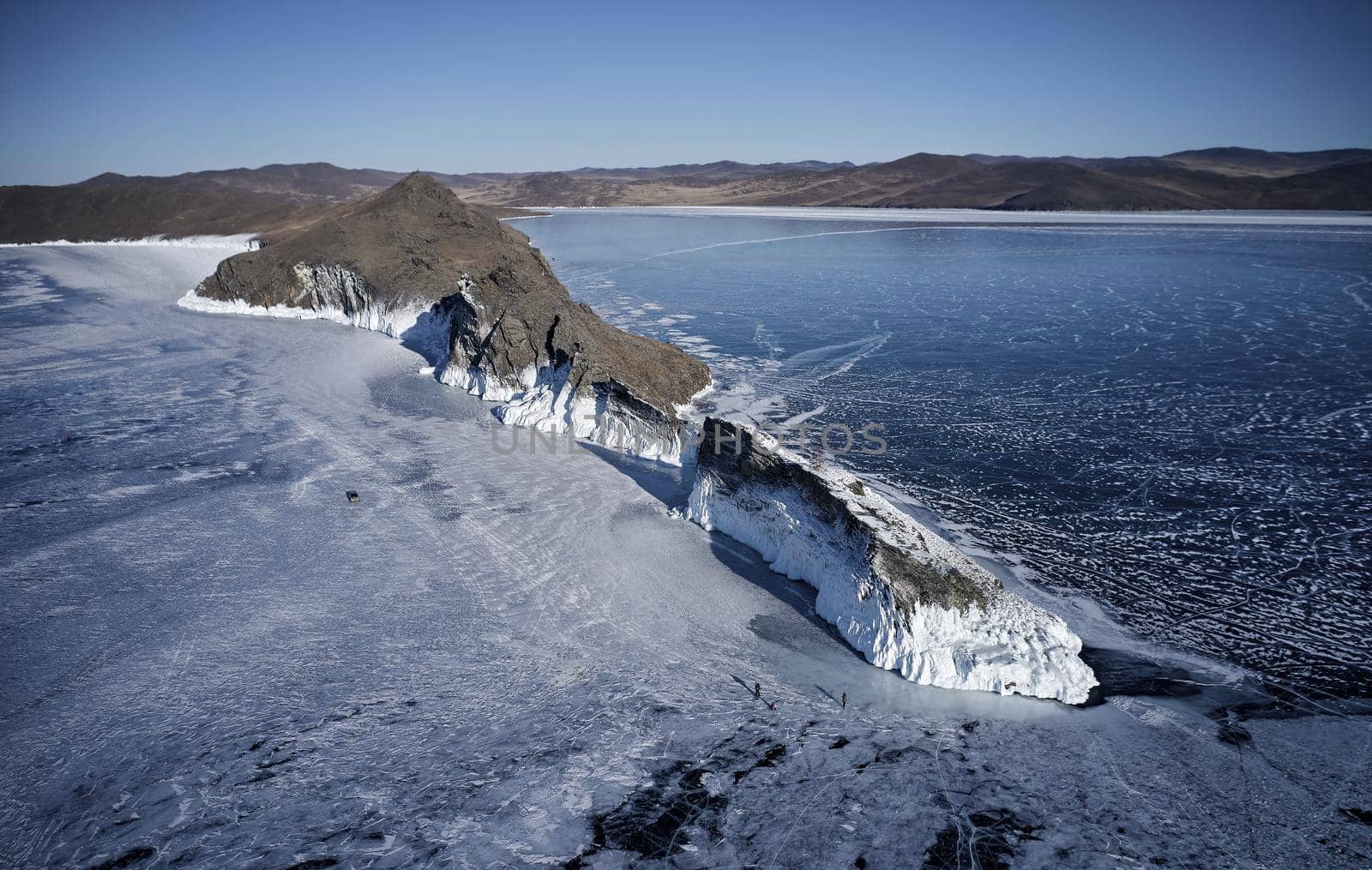 Frozen Lake Baikal, cape Horin-Irgi of Olkhon Island. Beautiful winter landscape with clear smooth ice near rocky shore. The famous natural landmark Russia. Blue transparent ice with deep cracks.