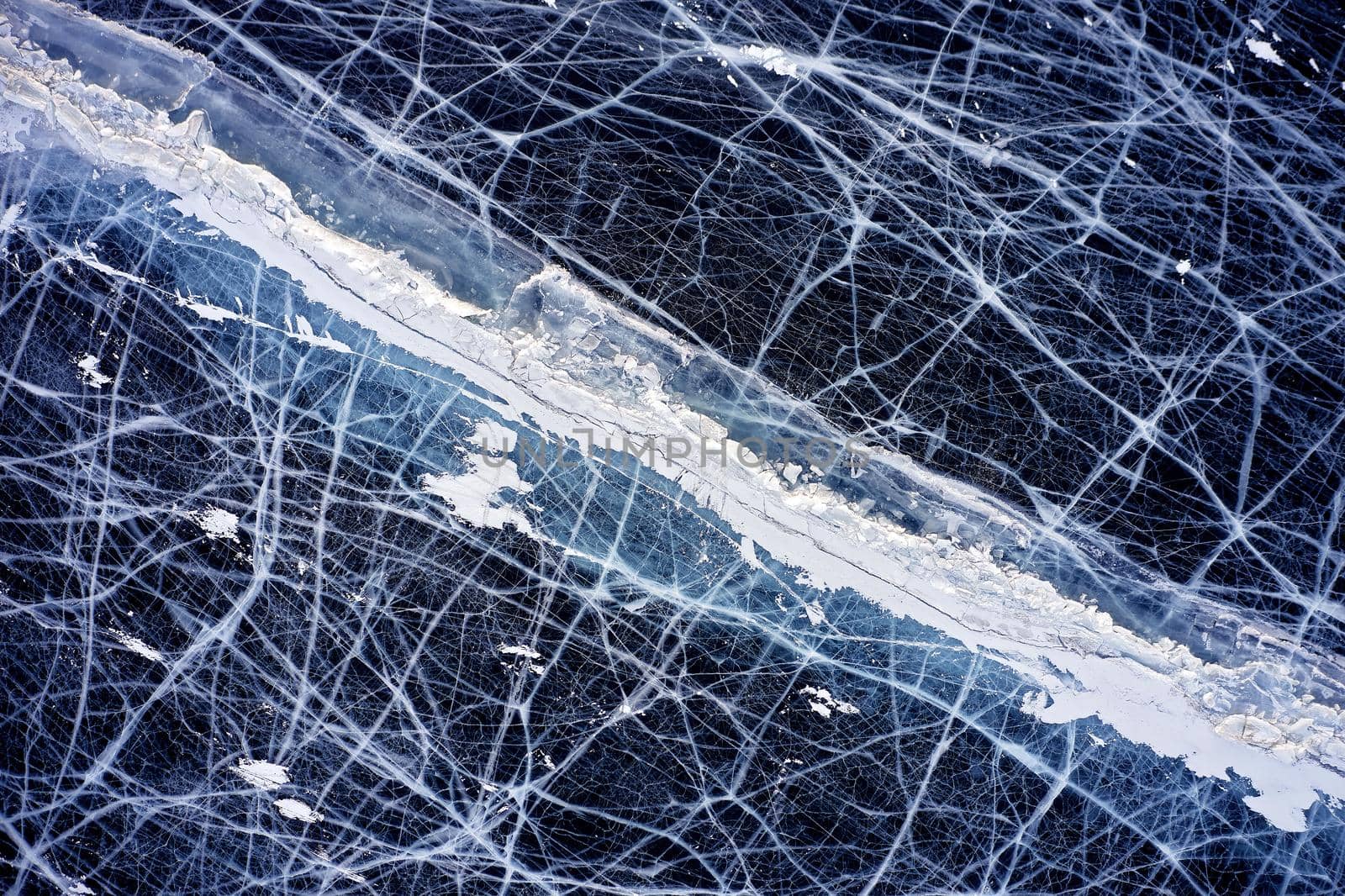 Frozen Lake Baikal, Aerial view. Beautiful winter landscape with clear smooth ice. Famous natural landmark Russia. Blue transparent ice with deep cracks, top view of a frozen lake.