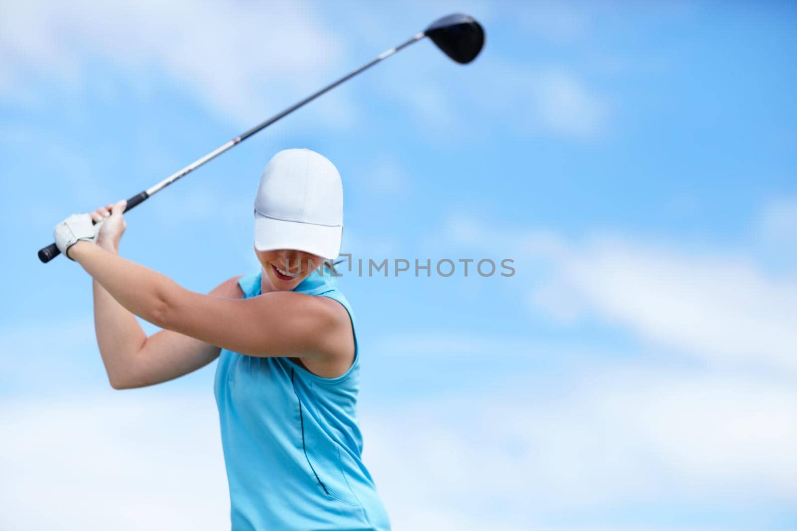 A young female golfer swinging a golf club (driver) over her head about to take a shot - copyspace.