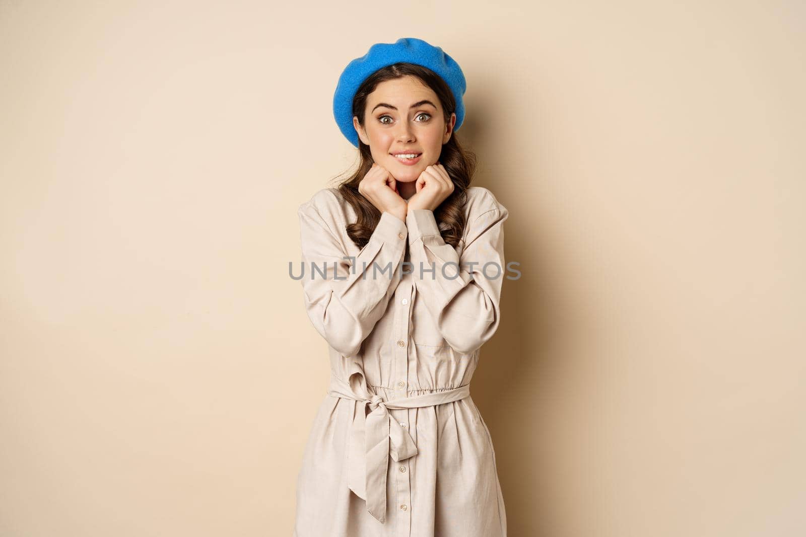 Portrait of beautiful woman in trendy outfit, touching her face and looking dreamy, yearning smth, standing against beige background by Benzoix