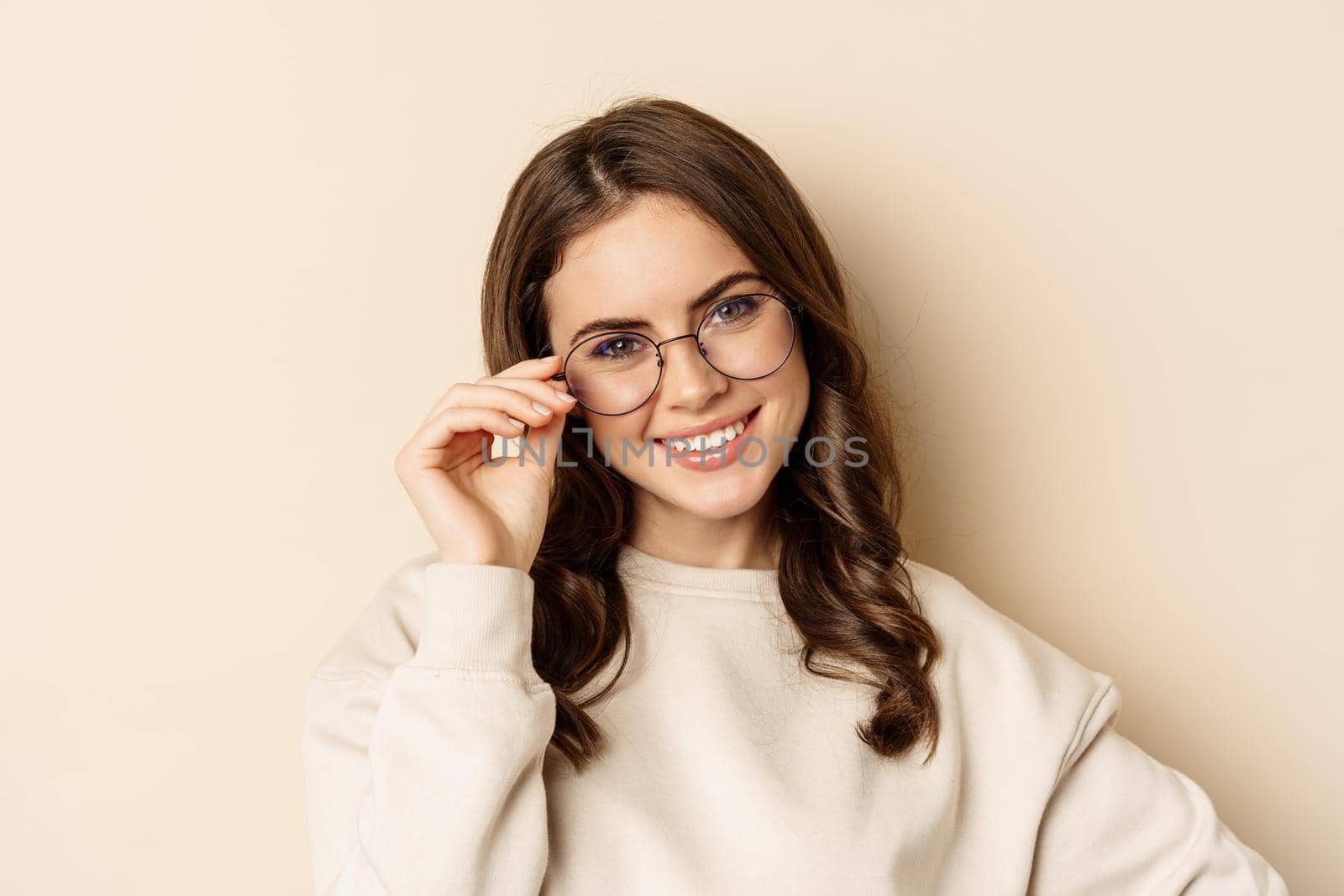 Stylish young caucasian woman wearing glasses and smiling, posing against beige background by Benzoix