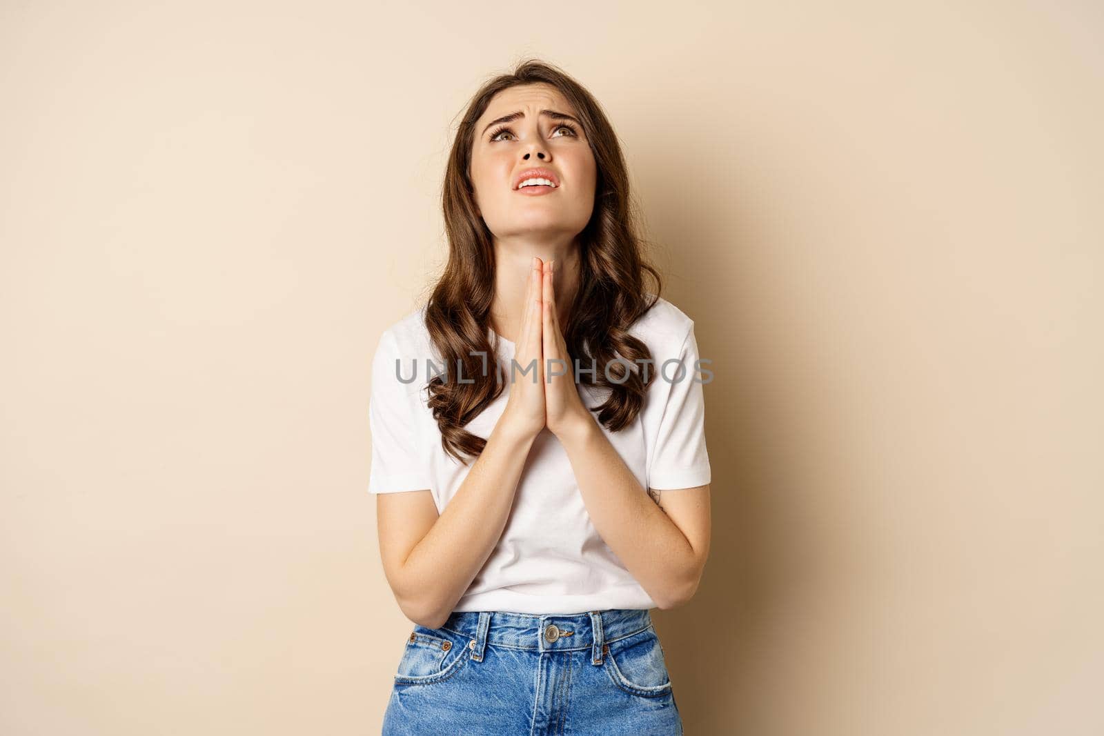 Woman pleading, begging and looking up desperate, need help, standing over beige background.