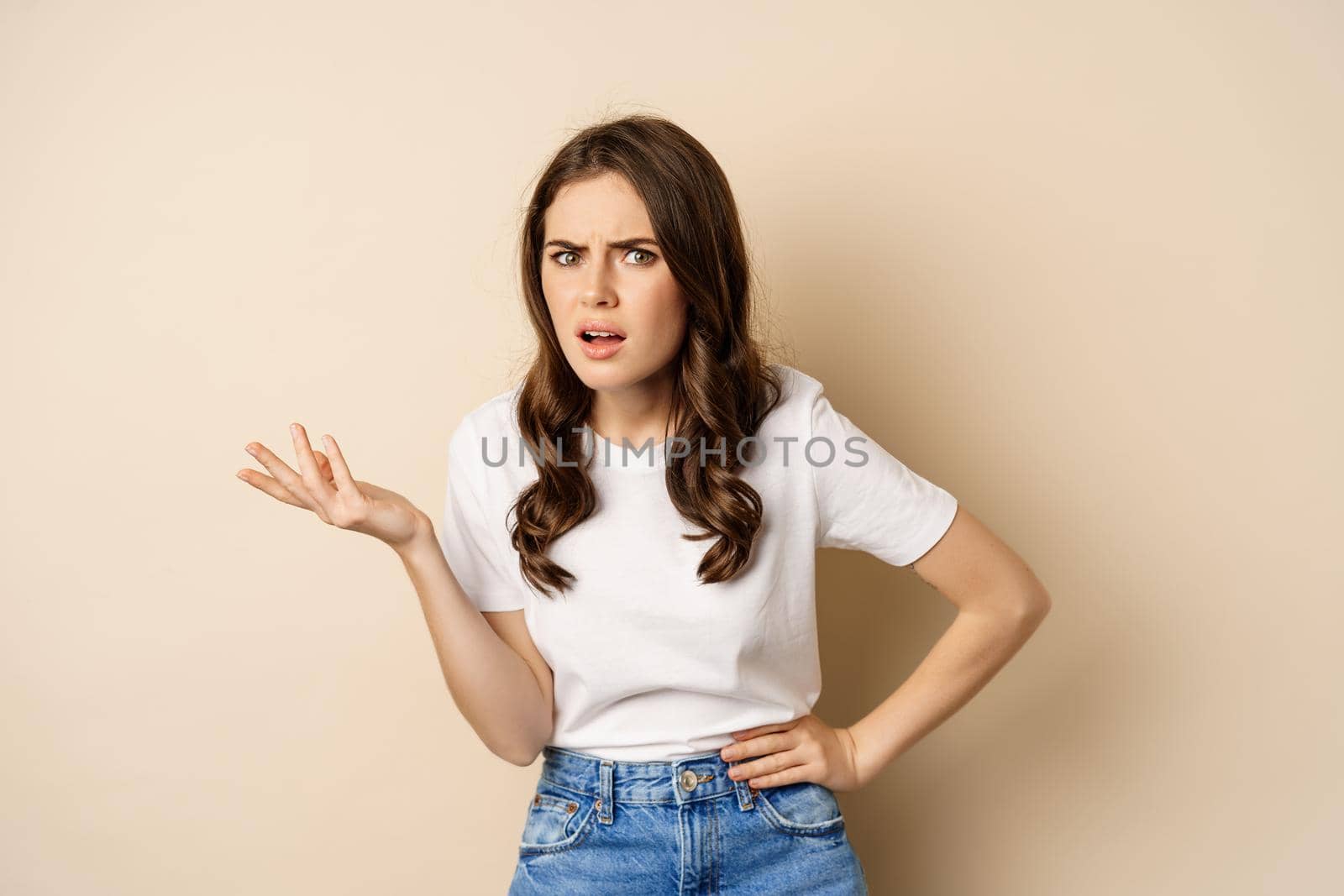 Confused woman looking clueless and annoyed, cant understand, asking whats problem, standing over beige background by Benzoix