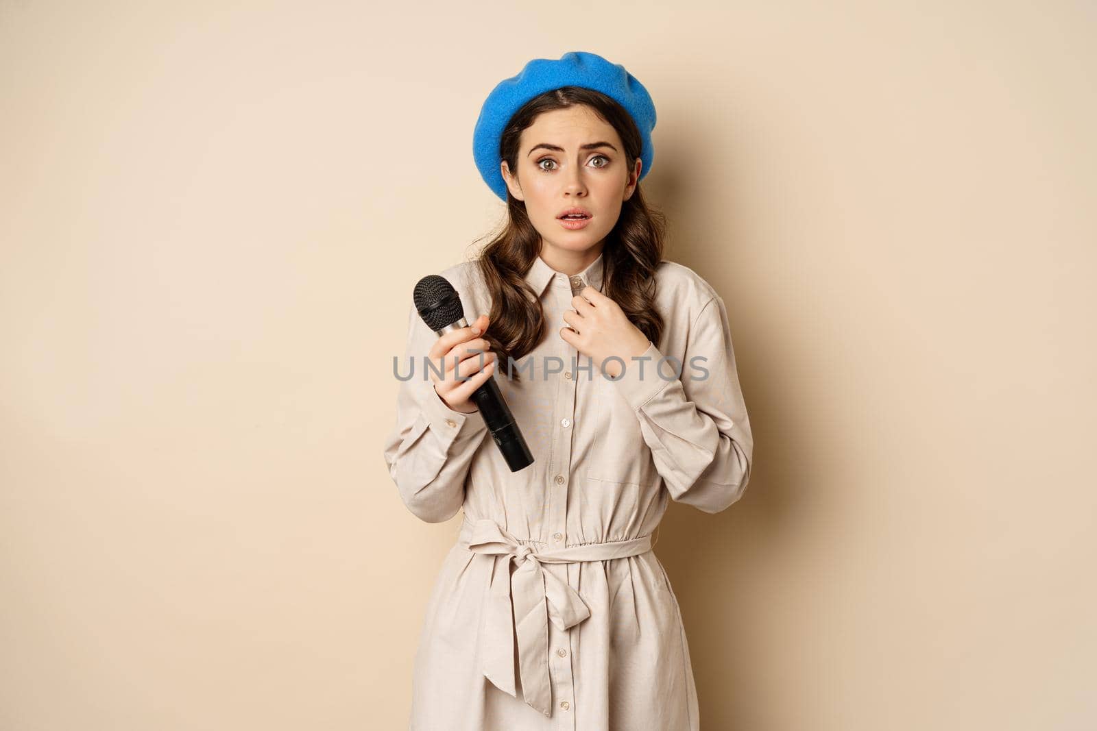 Stylish singer, woman with microphone touching throat, feeling ill, standing over beige background. Copy space