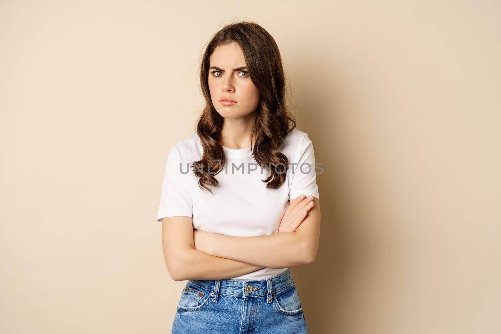 Offended angry woman cross hands on chest, frowning and sulking insulted, standing over beige background.