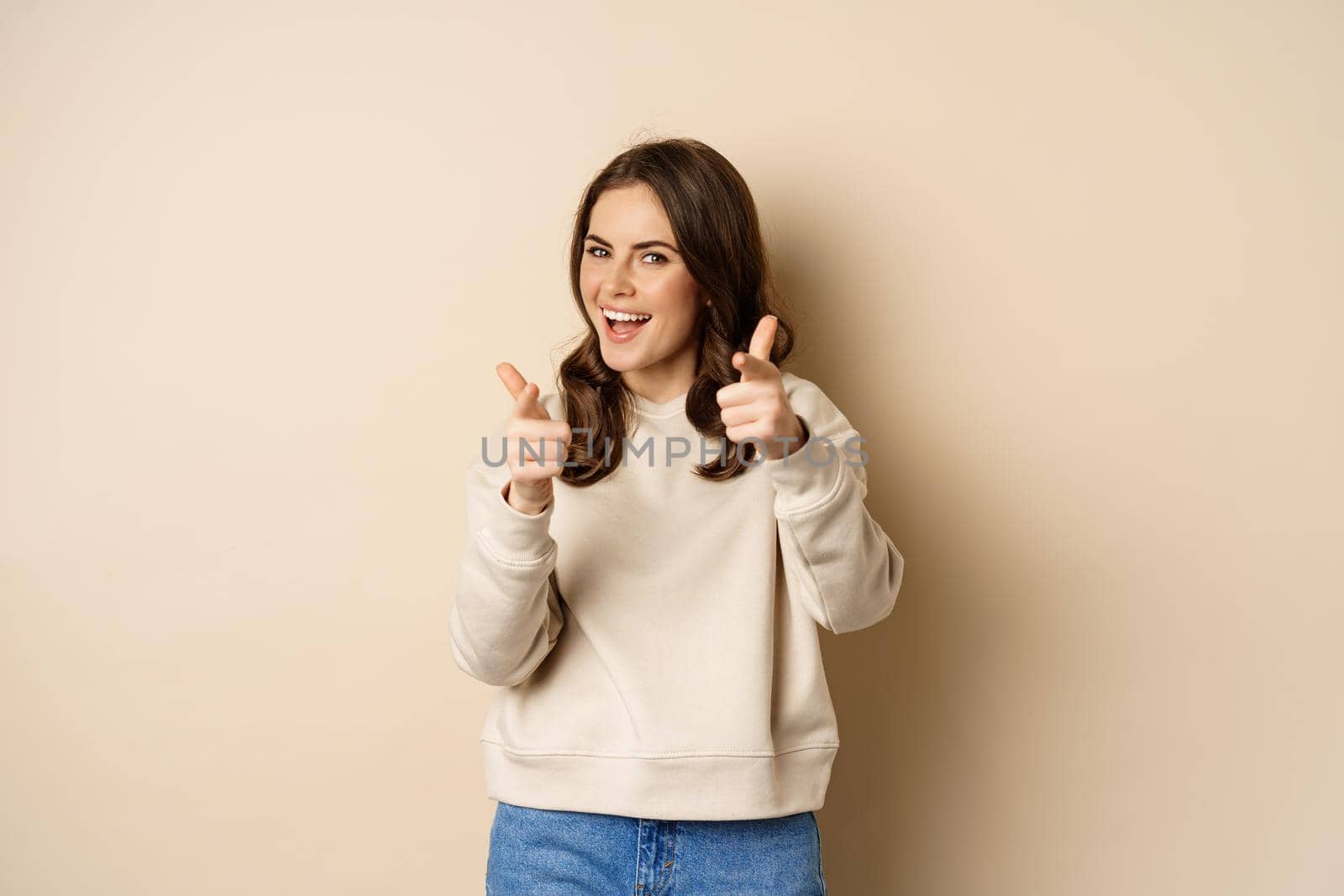 You got this. Happy young woman pointing fingers at camera, praising, complimenting, congrats gesture, standing over beige background by Benzoix