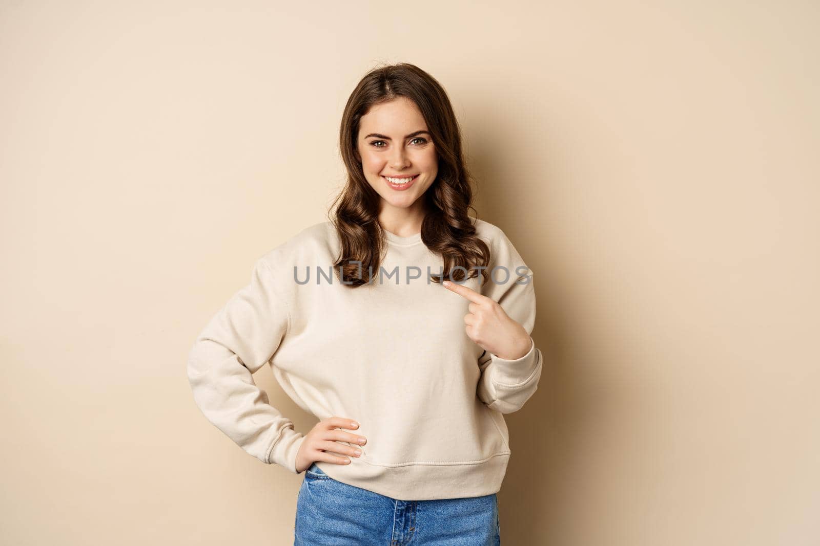 Confident smiling modern woman pointing finger at herself, self-promoting, standing over beige background by Benzoix