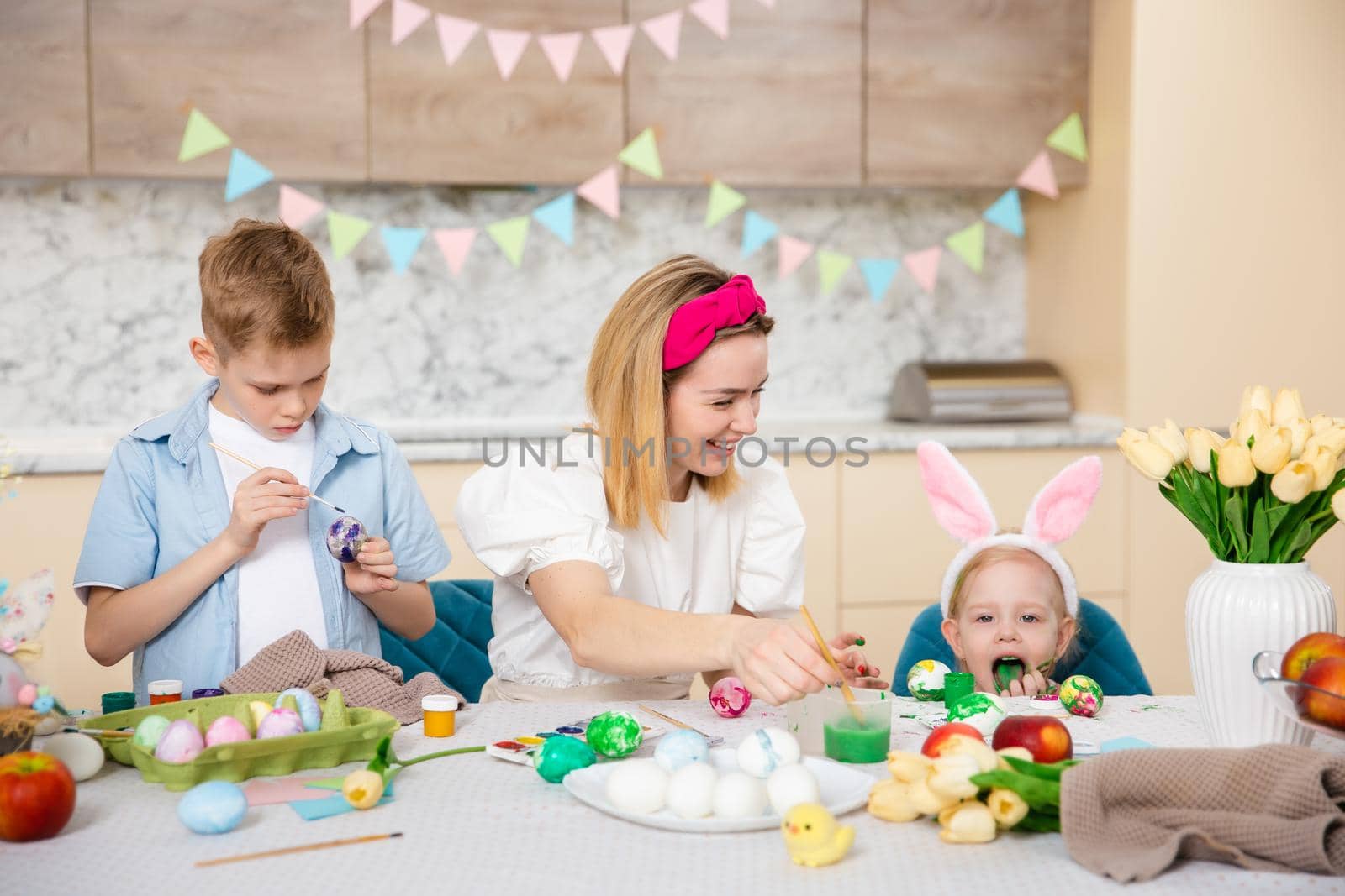 Happy Family preparing for Easter. Cute children with mother painting eggs. Home activity. Concept of unity and love. Mom, son, daughter. Brother and sister by Marina-A