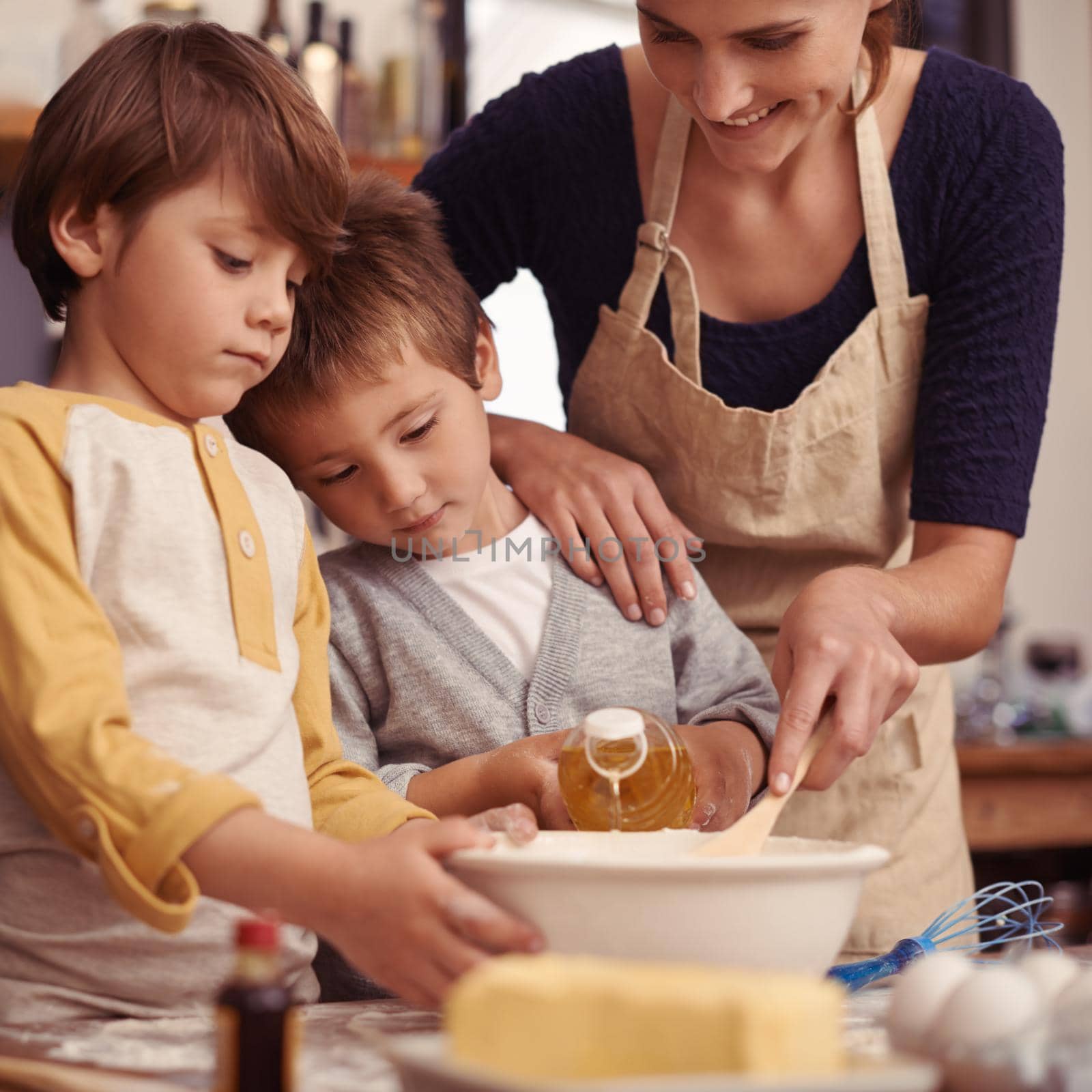 Two cute little boys baking with their mother in the kitchen.