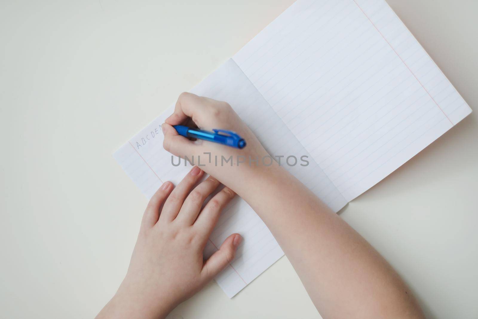 pupil's hands writing in open notebook, top view, copy space.