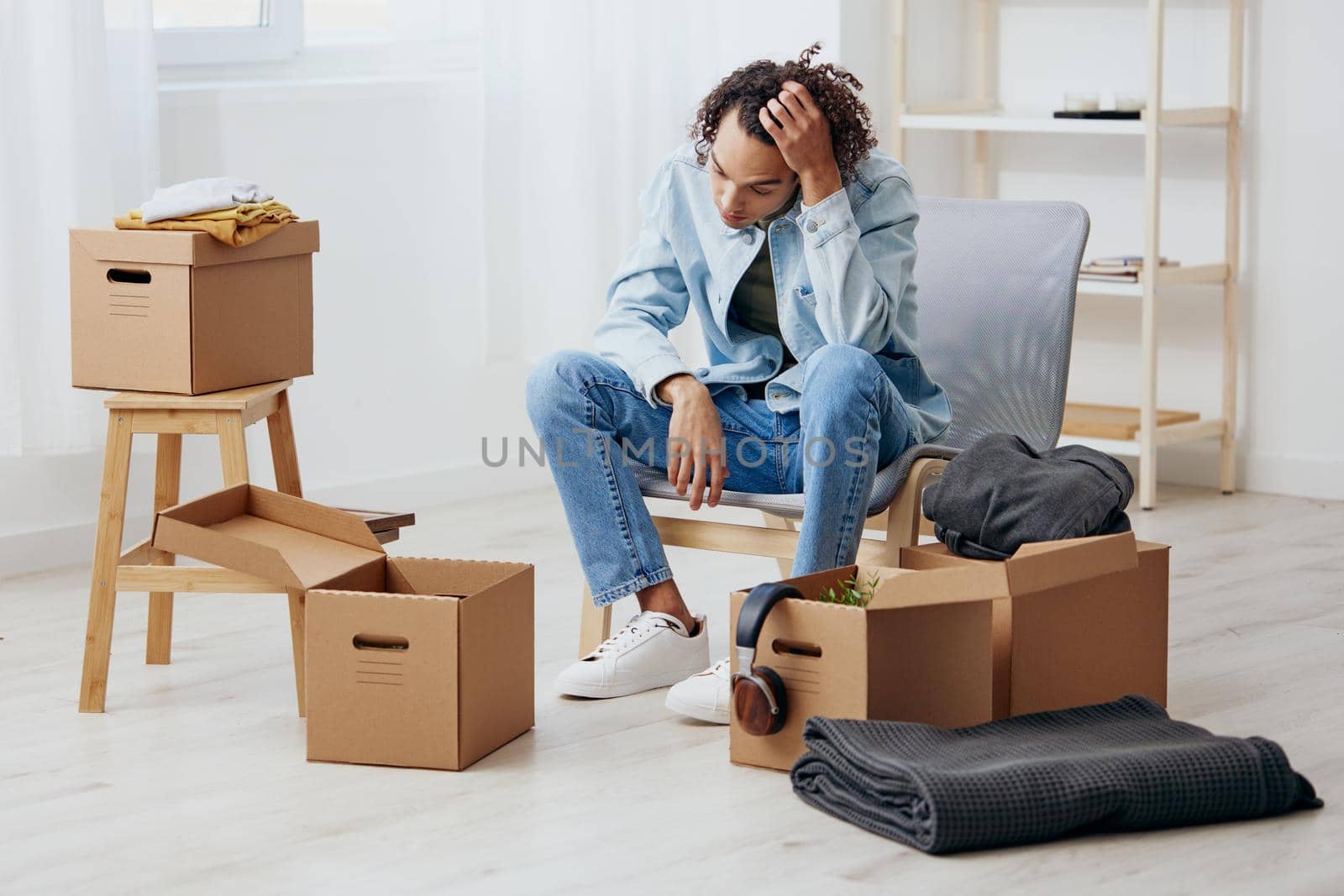 guy with curly hair sitting on a chair unpacking with box in hand moving Lifestyle by SHOTPRIME