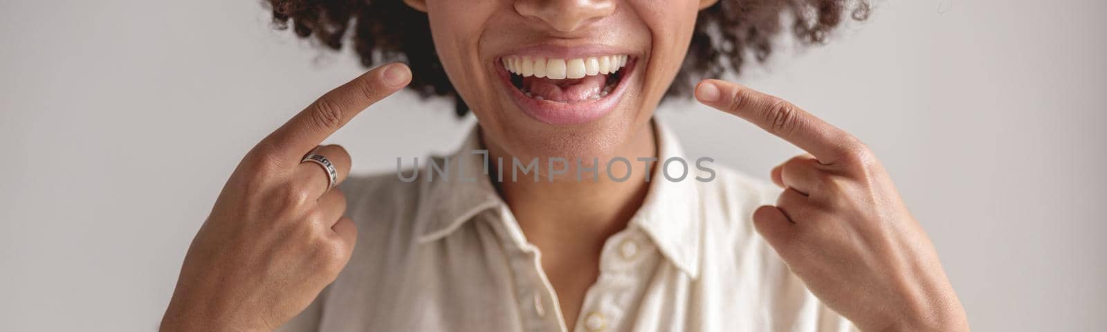 Cropped photo of happy African American woman pointing her fingers at smile, isolated on grey background