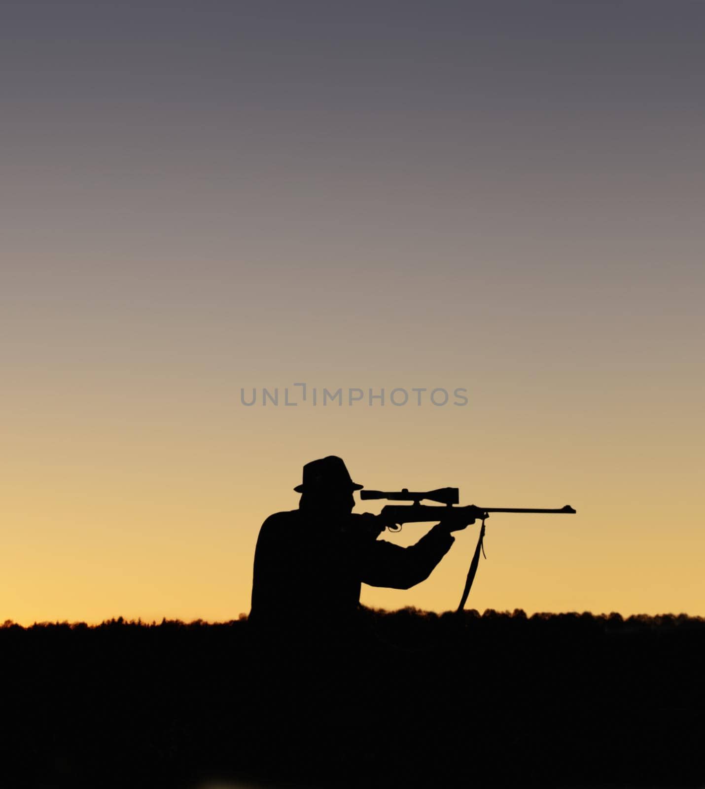 A silhouette of a man in the outdoors holding up his sniper rifle.