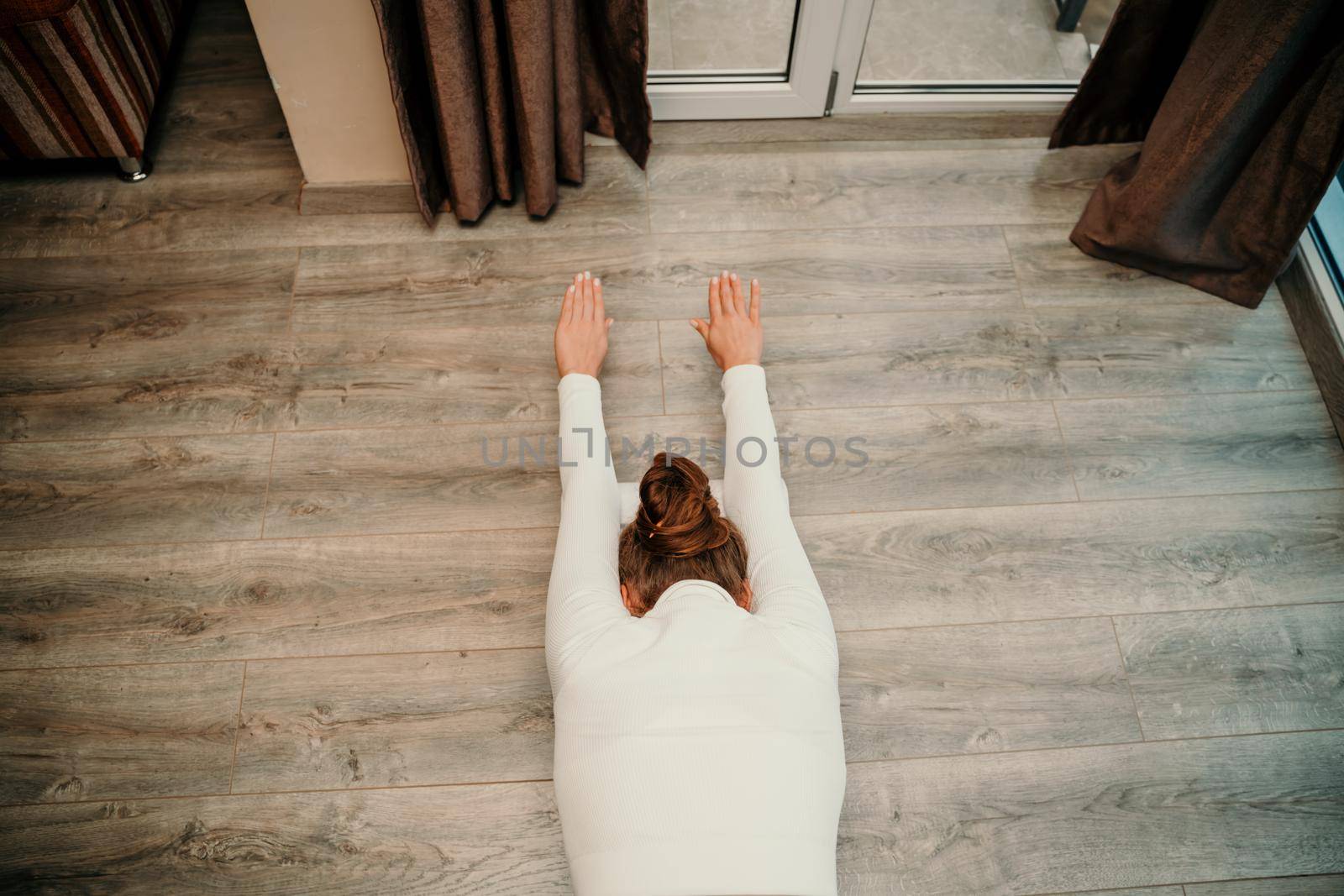 Adult athletic woman, in white bodysuit, performing fascia exercises on the floor - caucasian woman using a massage foam roller - a tool to relieve tension in the back and relieve muscle pain - the concept of physiotherapy and stretching training.