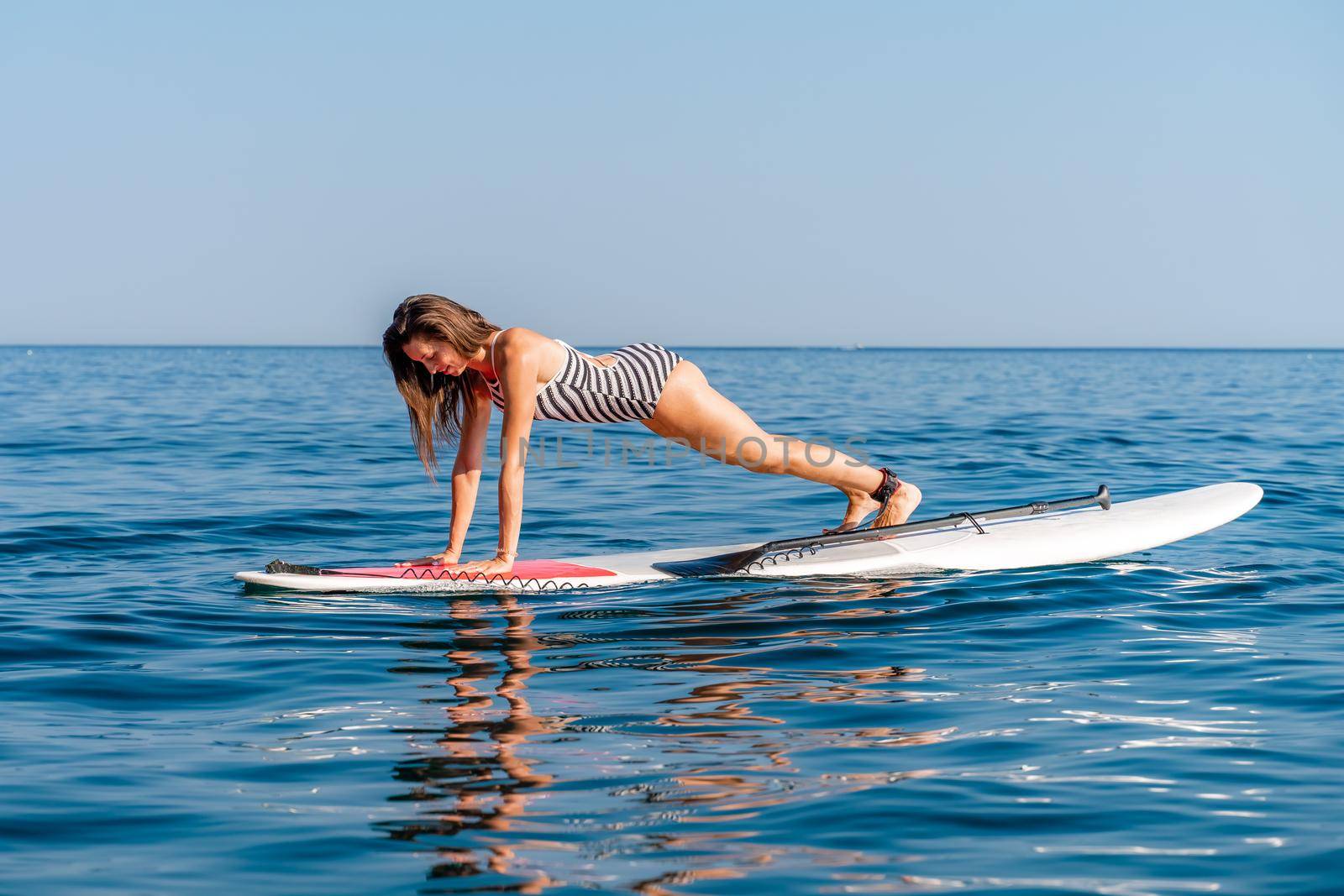 Sporty girl on a glanders surfboard in the sea on a sunny summer day. In a striped swimsuit, it is in the bar. Summer activities by Stortom by the sea by Matiunina