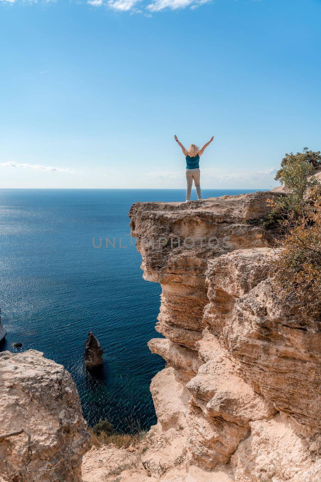 The woman at the top of the mountain raised her hands up on blue sky background. The woman climbed to the top and enjoyed her success. Back view