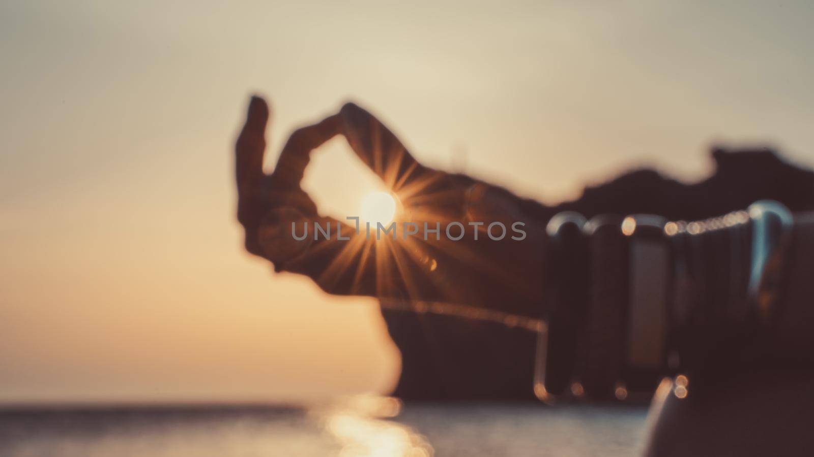 Banner. In blur closeup the hand of a young woman in bracelets. Practicing yoga on the beach with sunset. Keeps fingers connected, the sun shines through them. The concept of a healthy lifestyle, harmony. by Matiunina