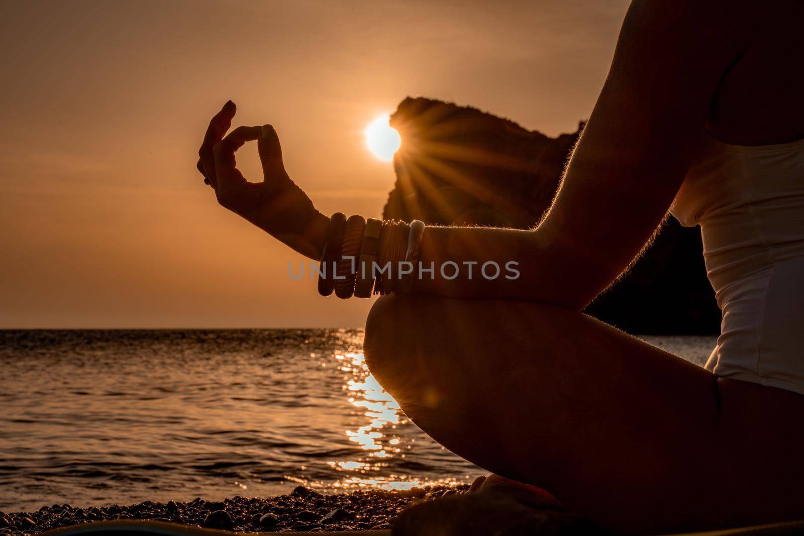 Young woman practicing yoga on the beach with sunset. Keeps fingers connected, the sun shines through them. The concept of a healthy lifestyle, harmony. by Matiunina