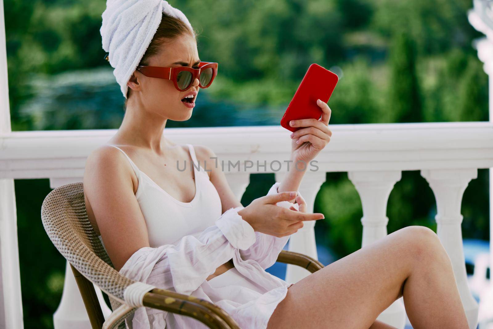 Portrait of young woman in sunglasses sits on the balcony and uses the phone Perfect sunny morning by SHOTPRIME