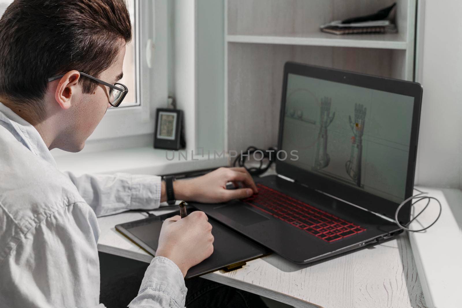 Young student male 3D designer uses graphics tablet to work at his desk. development of 3d characters for online games.