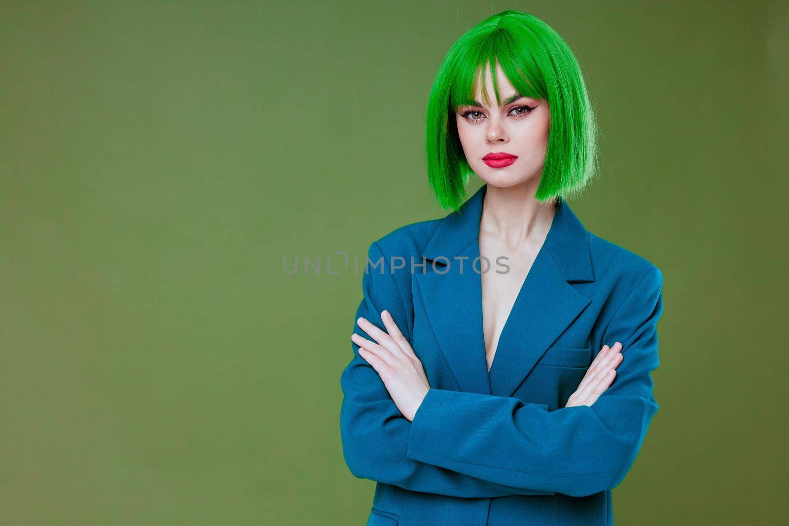 Positive young woman wearing a green wig blue jacket posing green background unaltered by SHOTPRIME