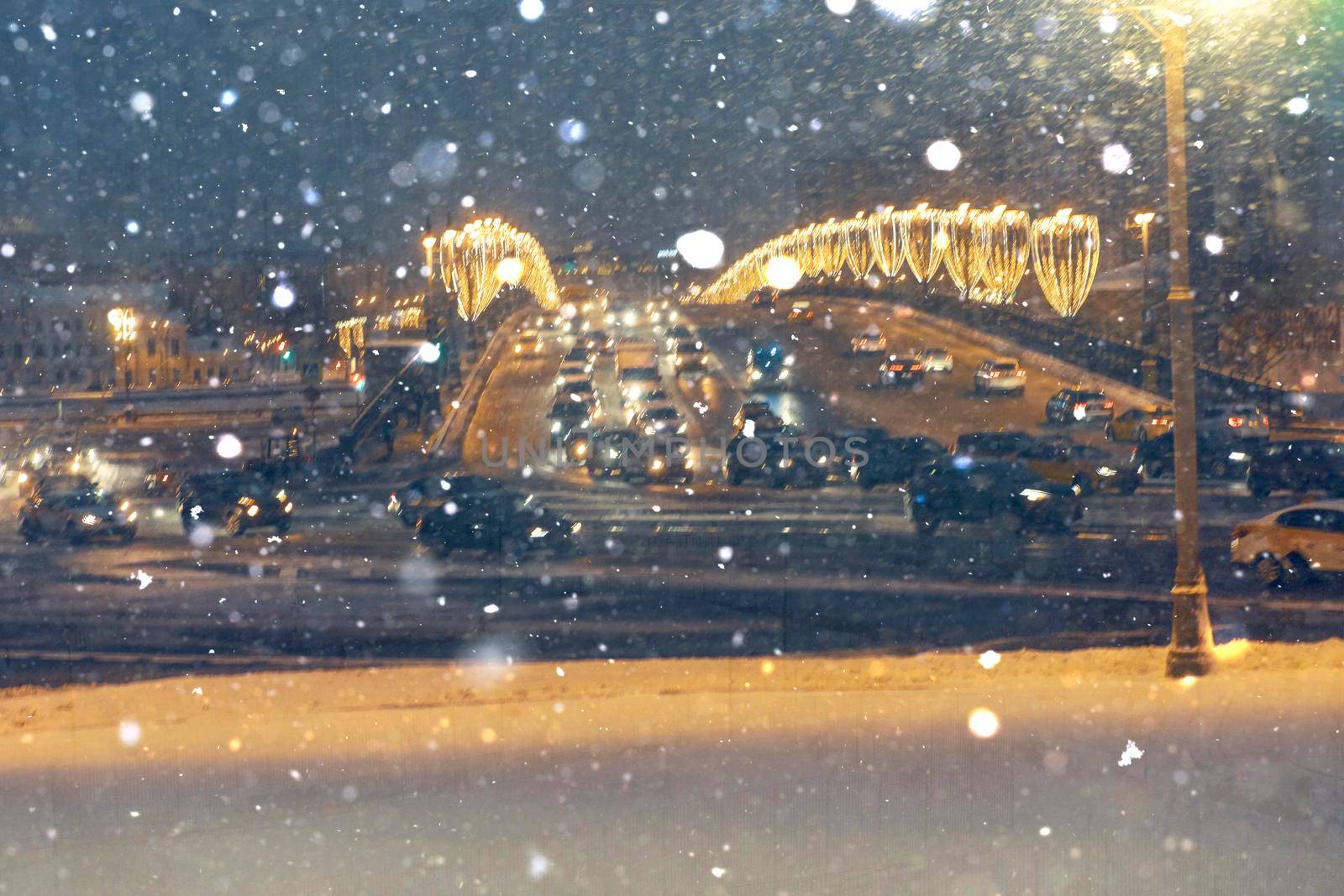Falling snow against the backdrop of cars with headlights on at night in the center of Moscow. The concept of the first snow or snowfall in winter.